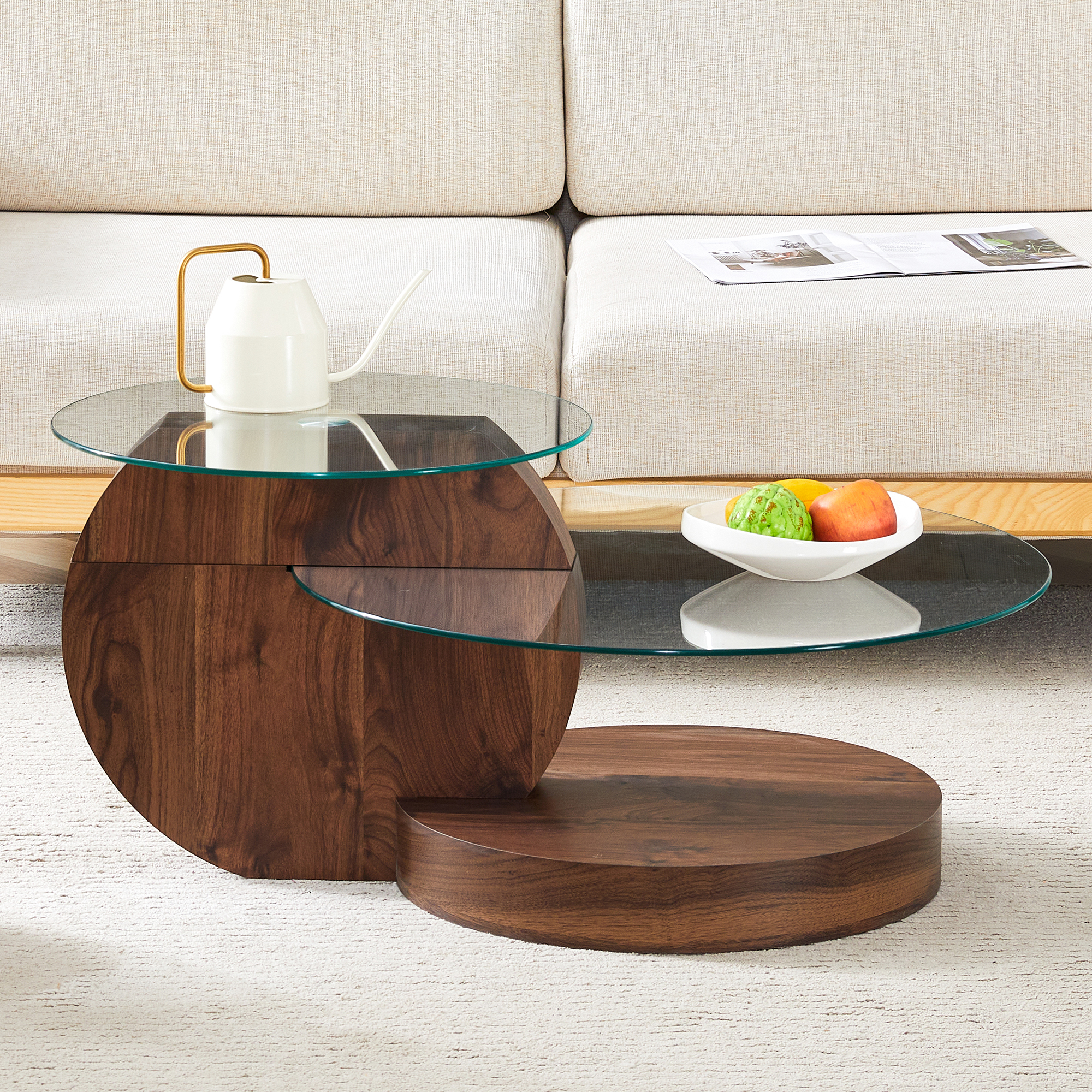 Ein runder Couchtisch aus Holz mit Glastopplatten, darauf eine weiße Kanne und Obst.