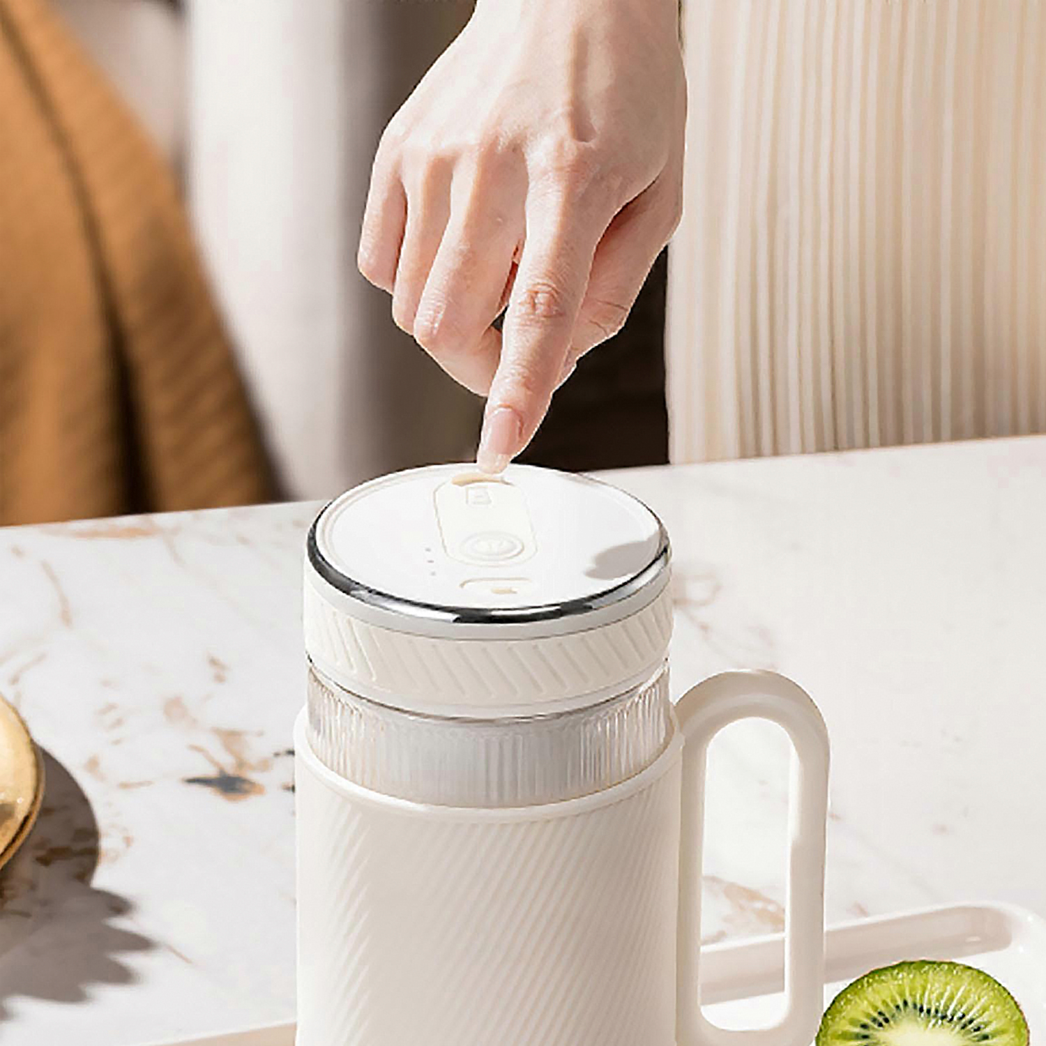 Una mano presiona un botón en una licuadora blanca. Una rodaja de kiwi está cerca.