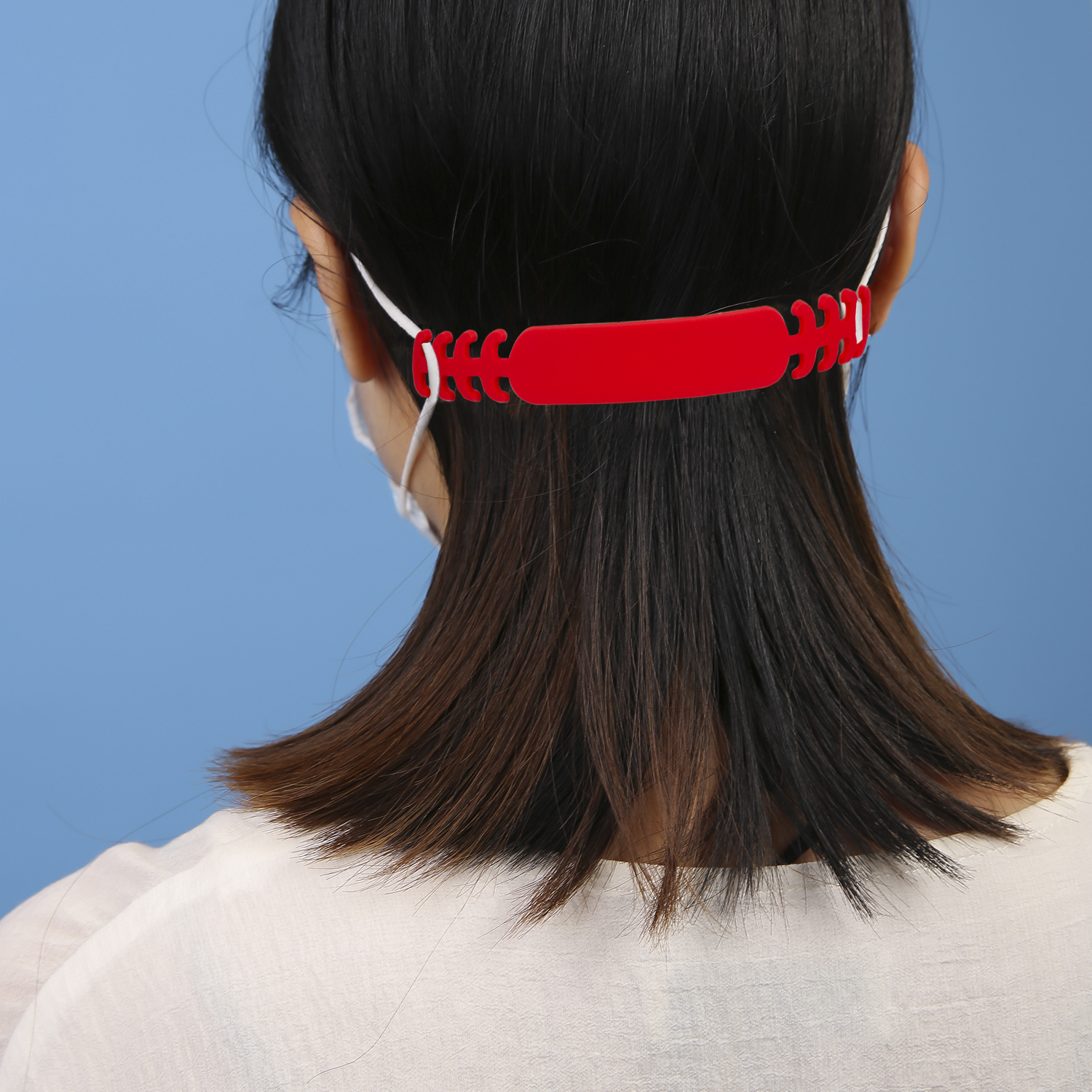Vista trasera de mujer con camisa blanca y mascarilla, con extensor de mascarilla rojo.