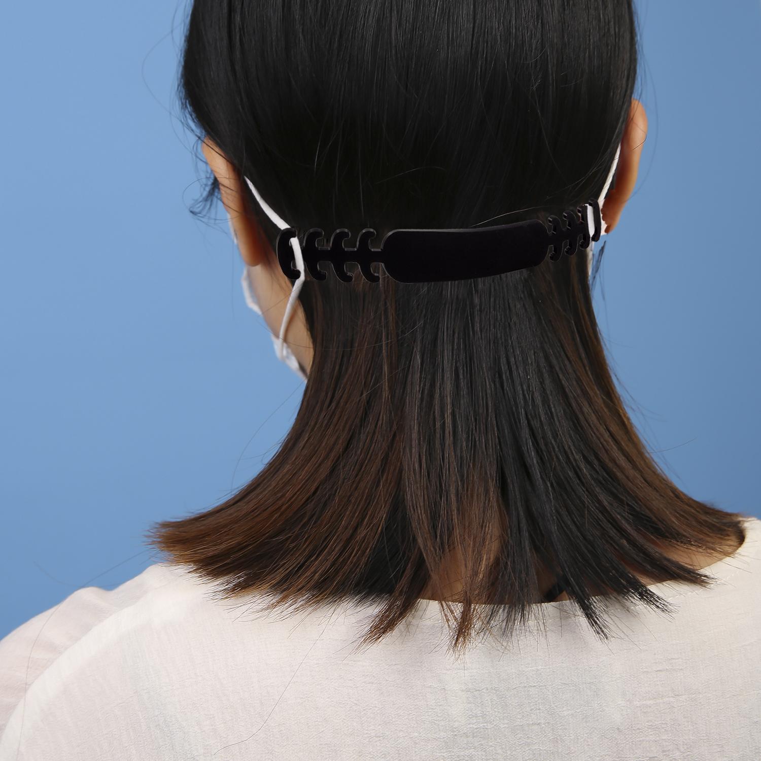 Vista trasera de una mujer con pelo negro usando mascarilla con sujetador de orejas.