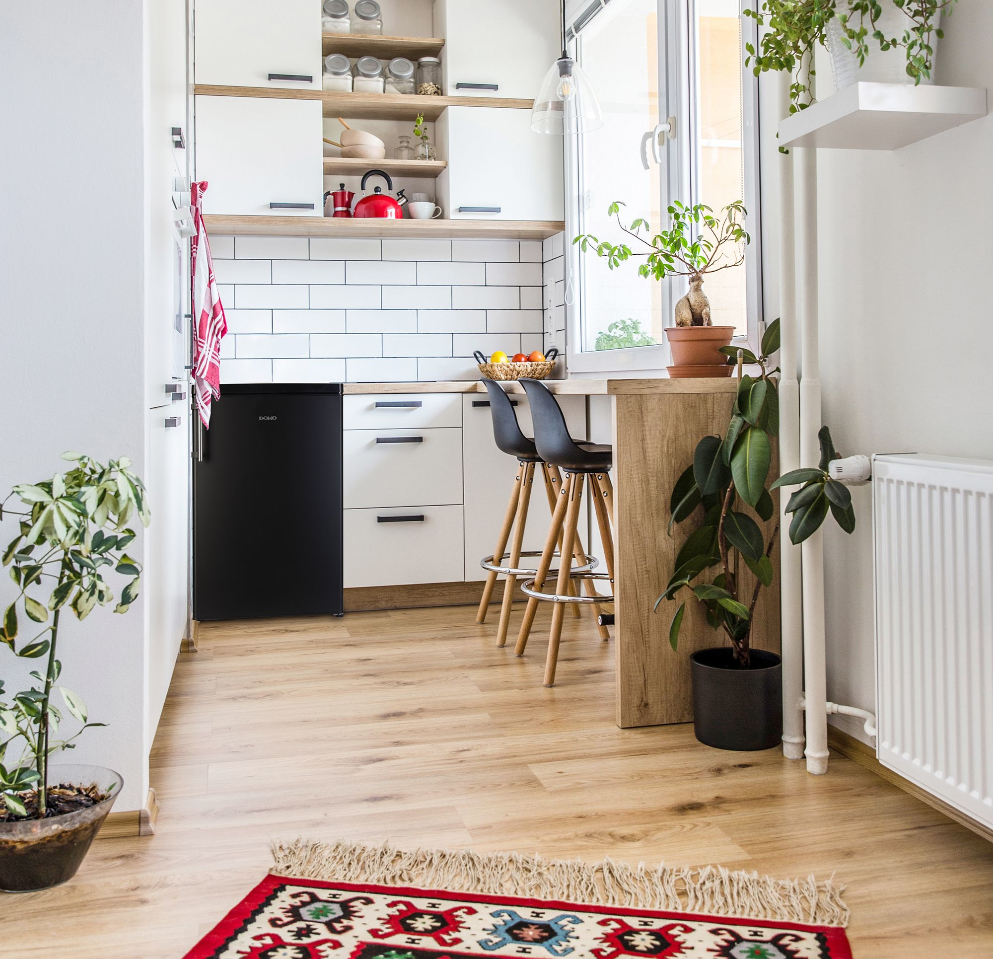 Kleine K&uuml;che mit schwarzen Mini-K&uuml;hlschrank, wei&szlig;en Schränken und Holzboden.