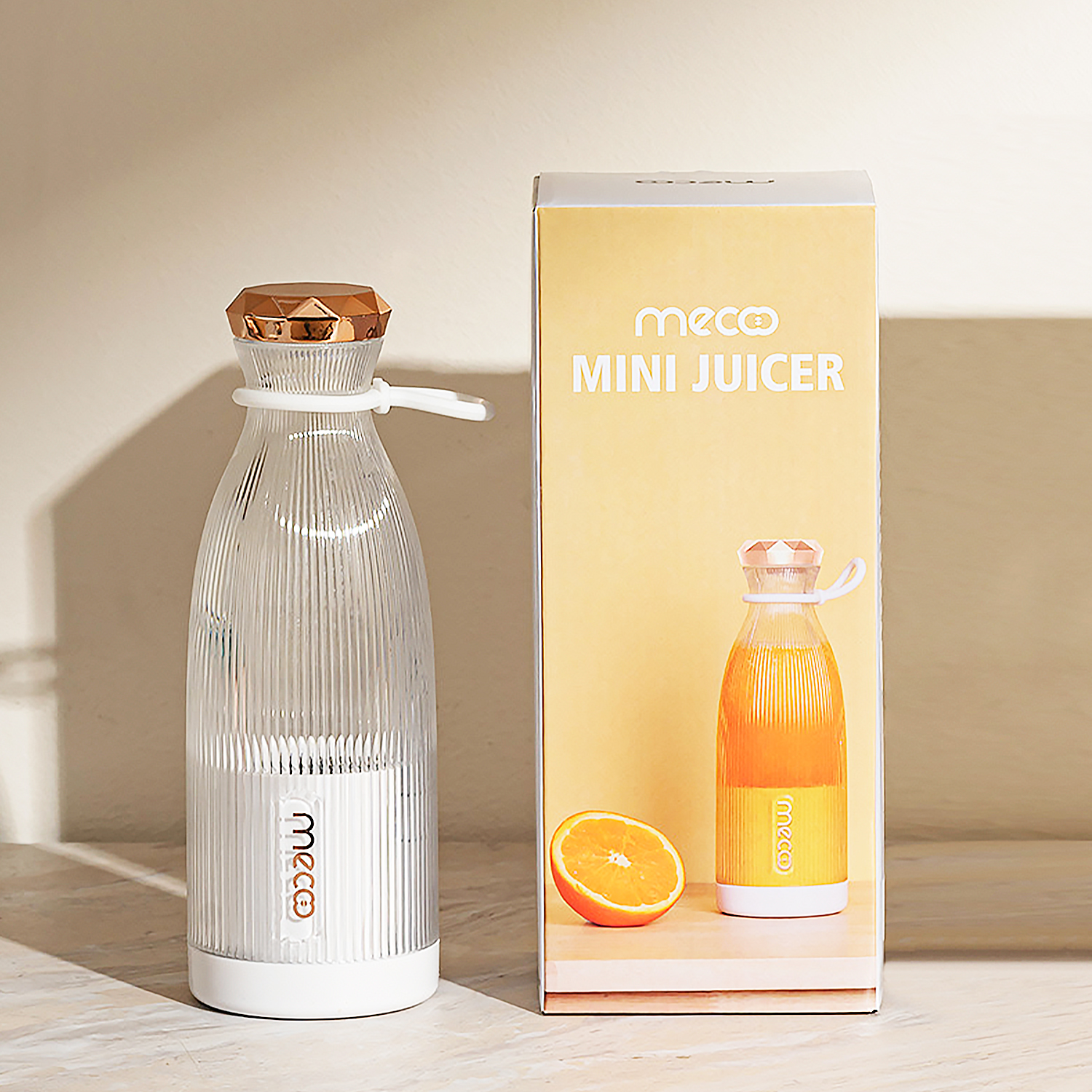 Un mini exprimidor transparente con tapa dorada y caja naranja.
