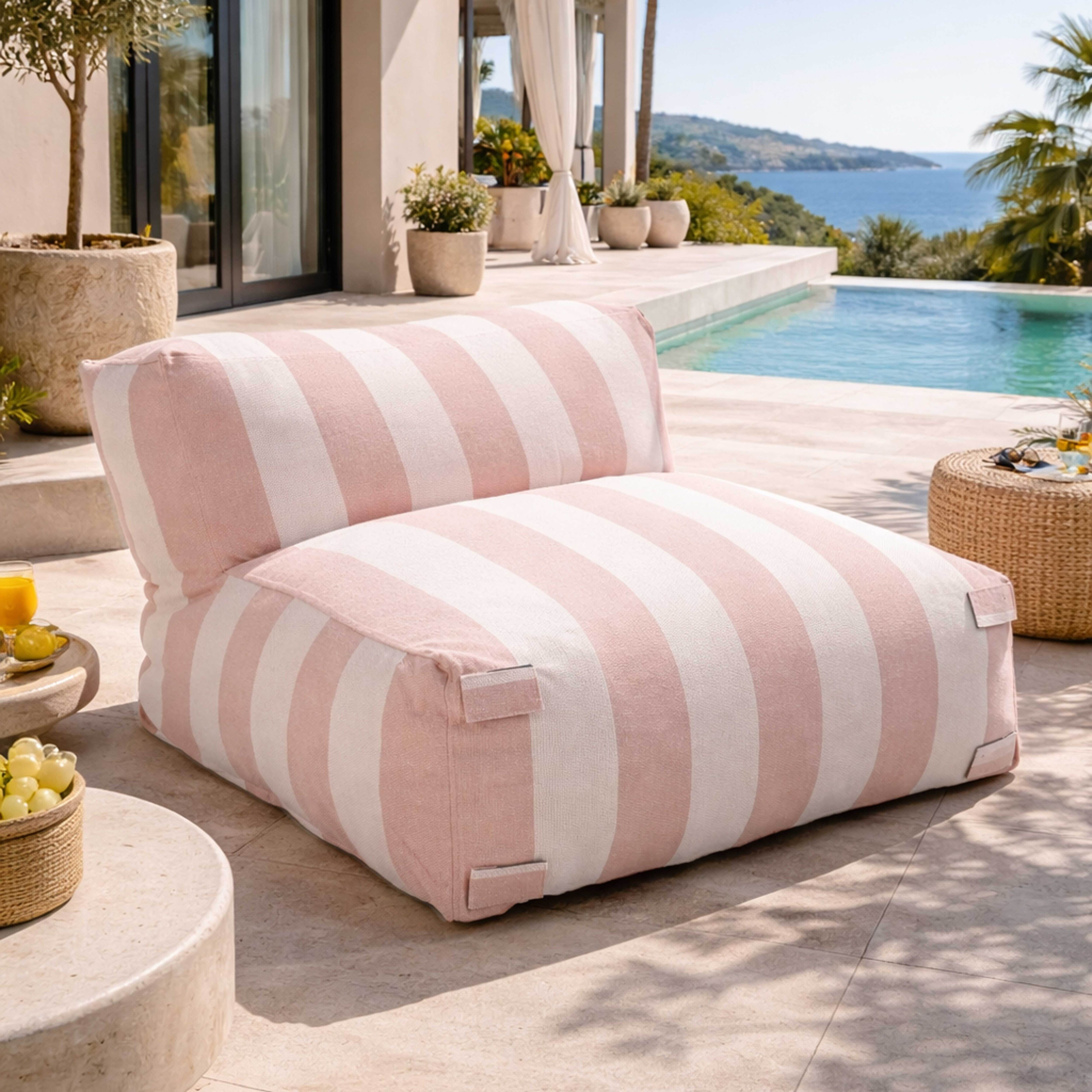 Ein rosafarbener gestreifter Sessel steht neben einem Pool mit Blick auf das Meer.