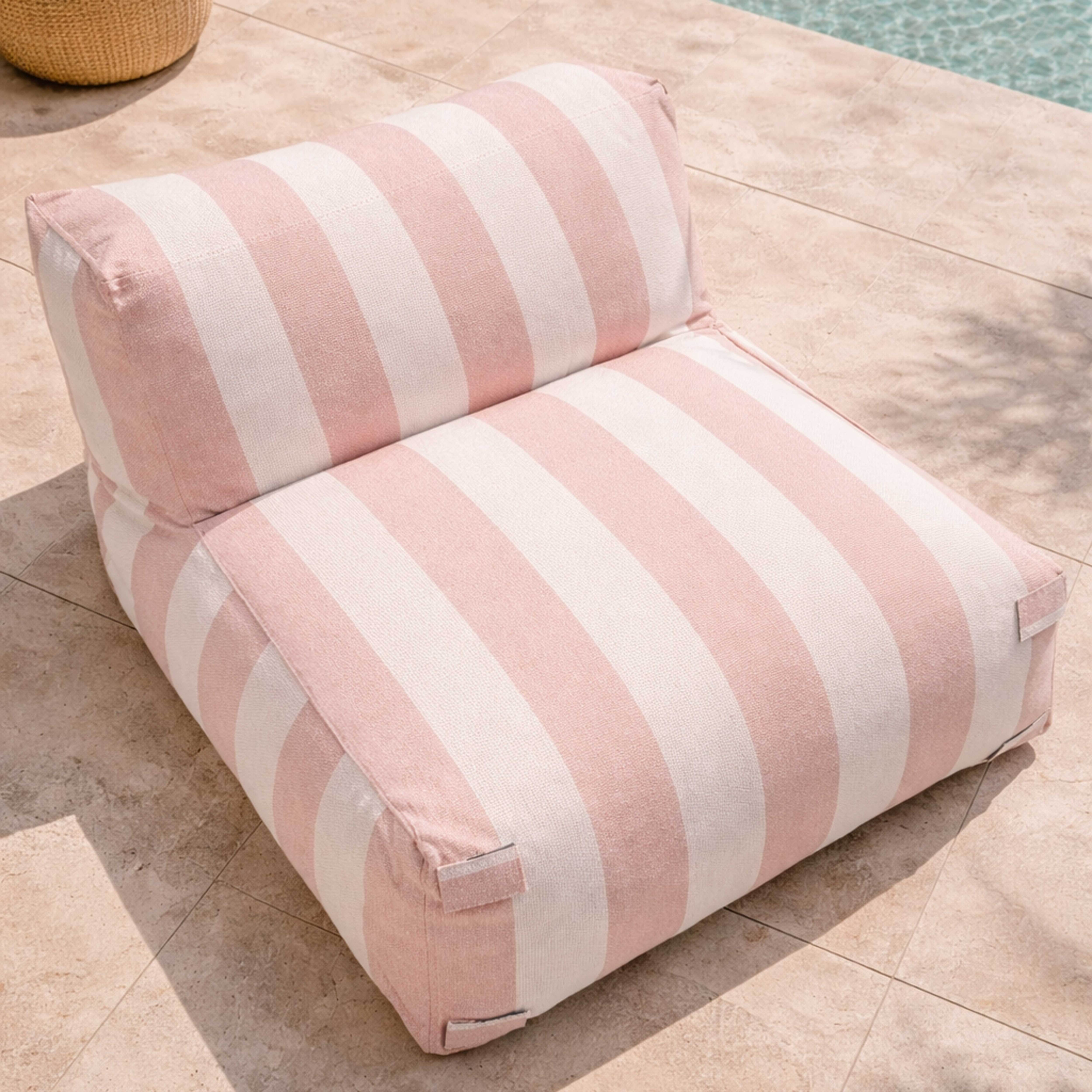Ein gestreifter Sitzsack in Rosa und Weiß liegt auf einer gefliesten Terrasse neben einem Pool.