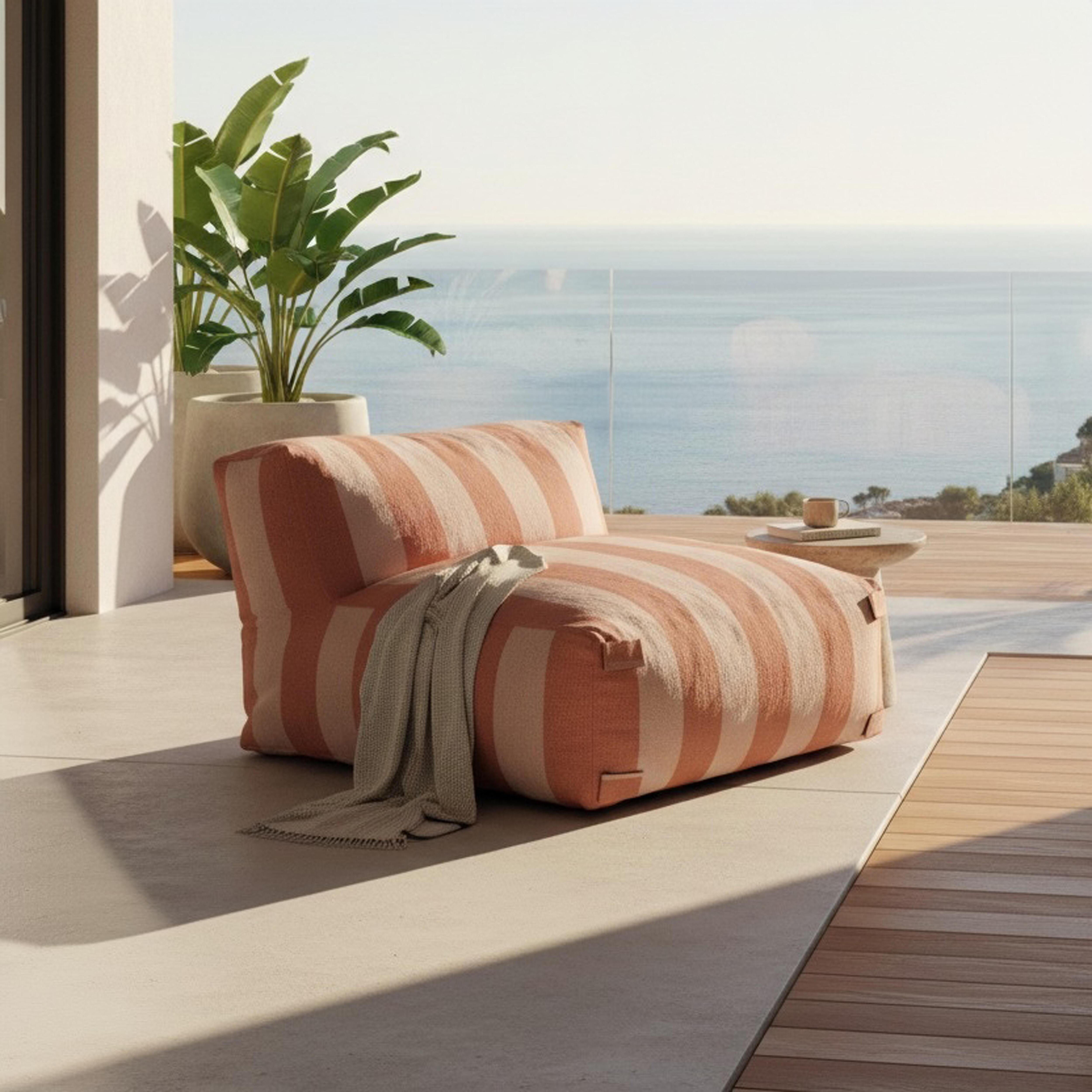 Ein gestreifter Sessel mit einer Decke steht auf einer Terrasse am Meer.