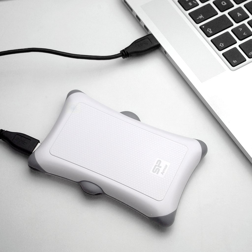 Biały dysk zewnętrzny z szarymi akcentami jest podłączony do laptopa przez USB.