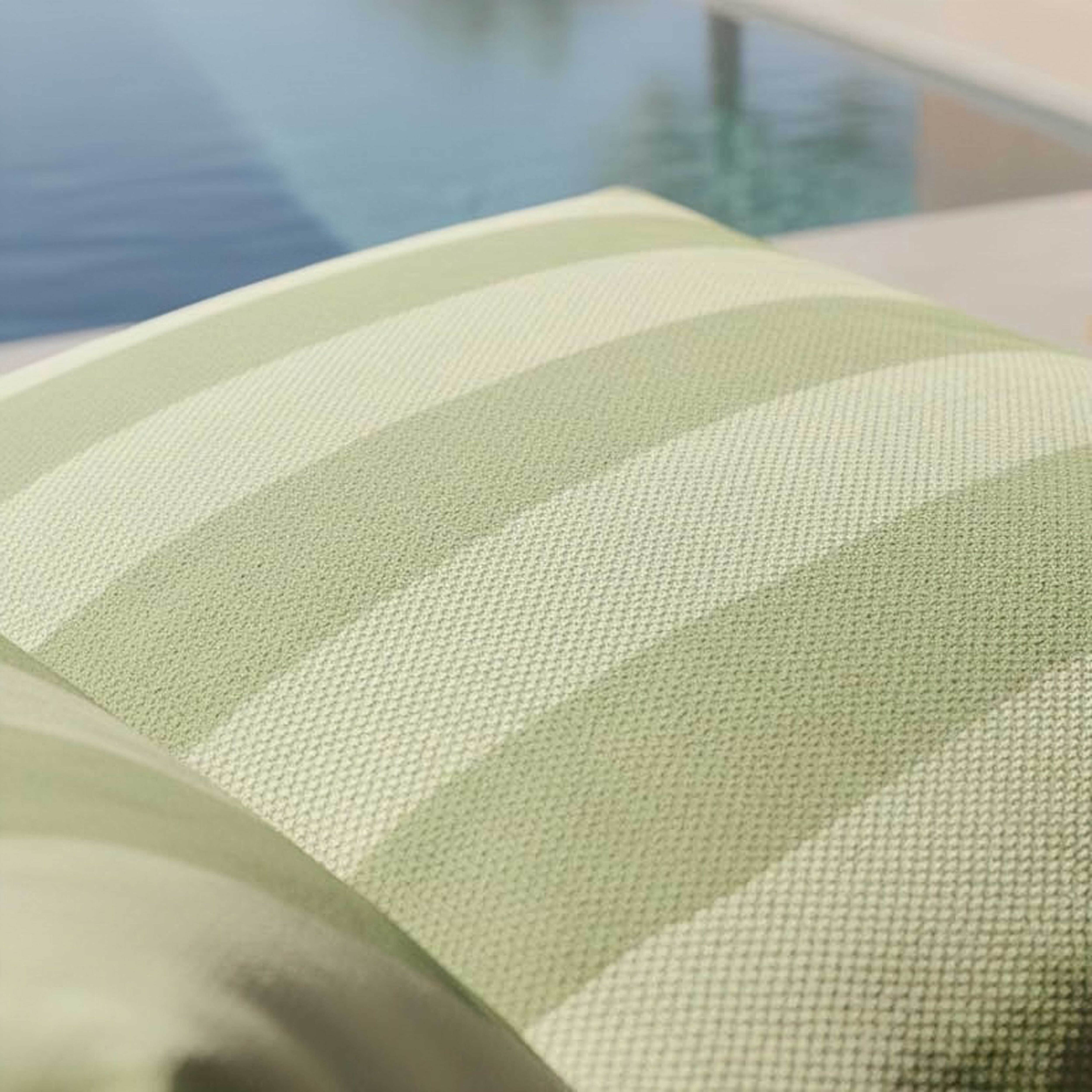 Ein grünes und weiß gestreiftes Kissen liegt neben einem Pool.