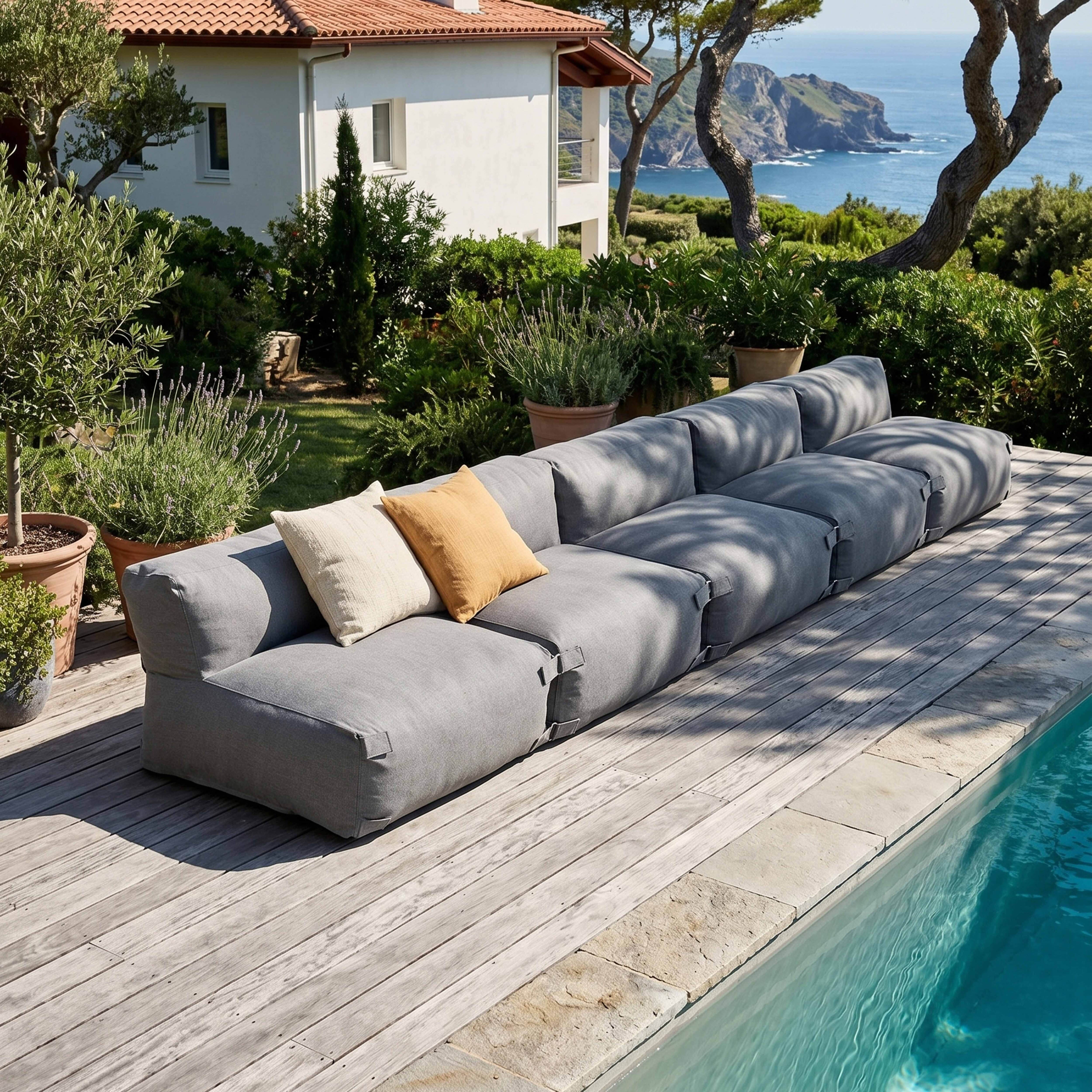 Ein langes graues Modulsofa mit zwei Kissen steht auf einer Holzterrasse am Pool.