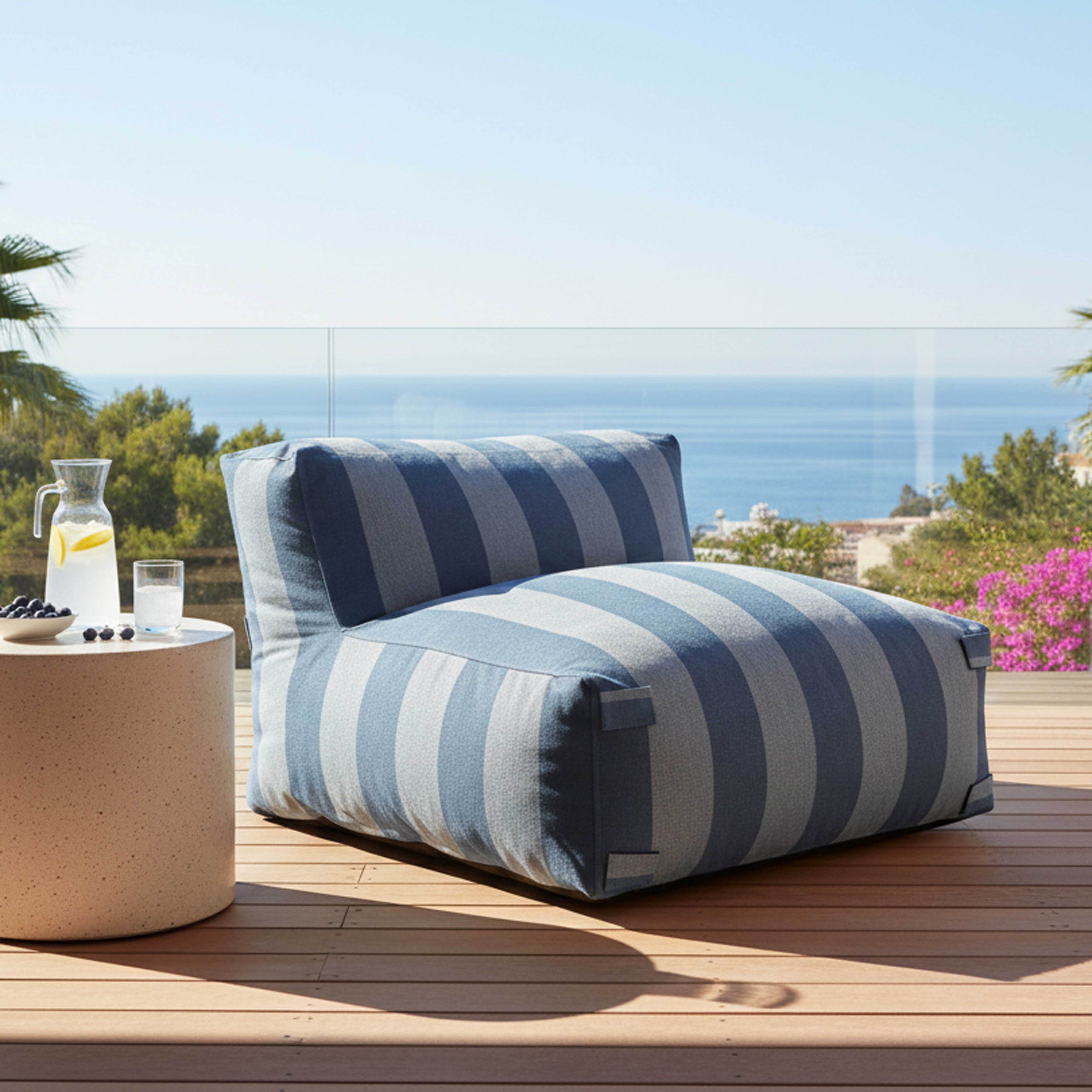 Ein gestreifter Outdoor-Sitzsack steht auf einer Holzterrasse mit Blick aufs Meer.