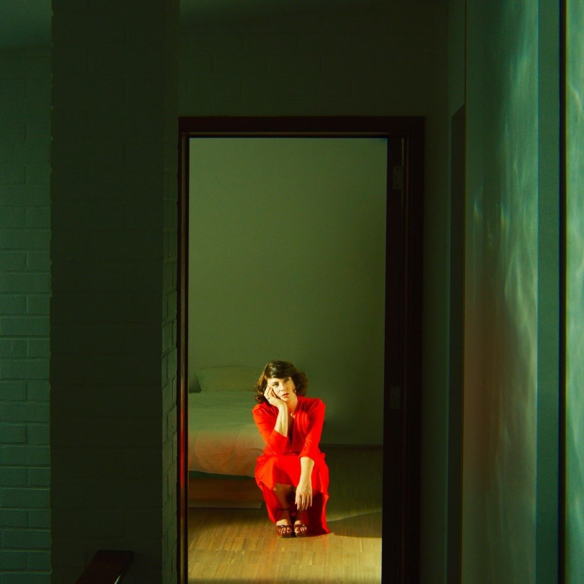 Una donna in abito rosso seduta sul pavimento davanti a un letto.