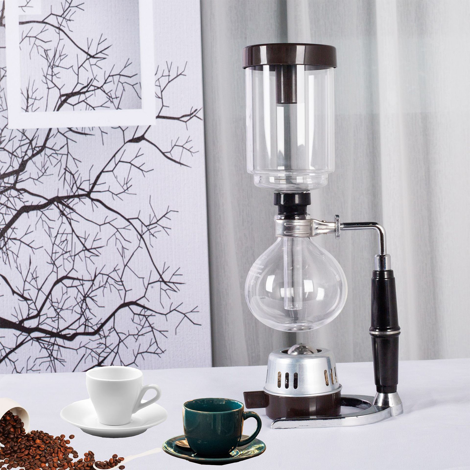 Una cafetera de sifón con dos tazas, granos de café y una obra de arte de árbol.