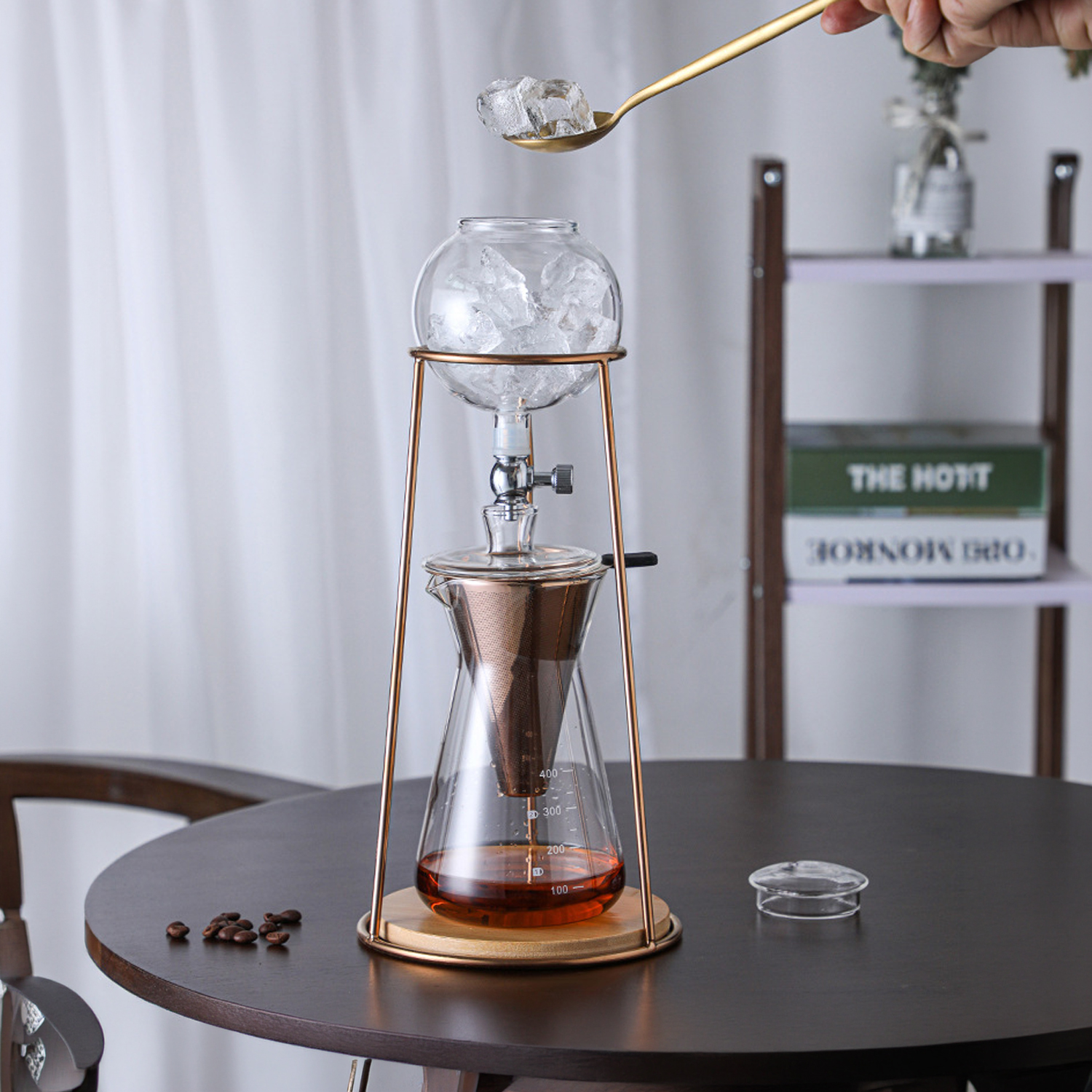 Una cafetera de goteo en frío de vidrio con hielo agregándose con una cuchara.