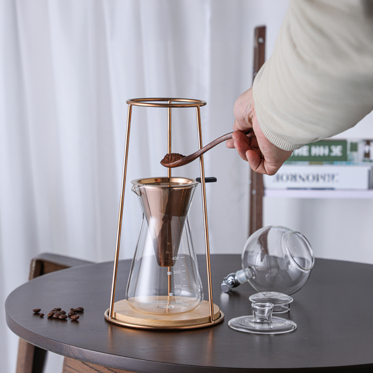 Una mano añade café molido con cuchara de madera a una cafetera de vertido de vidrio.