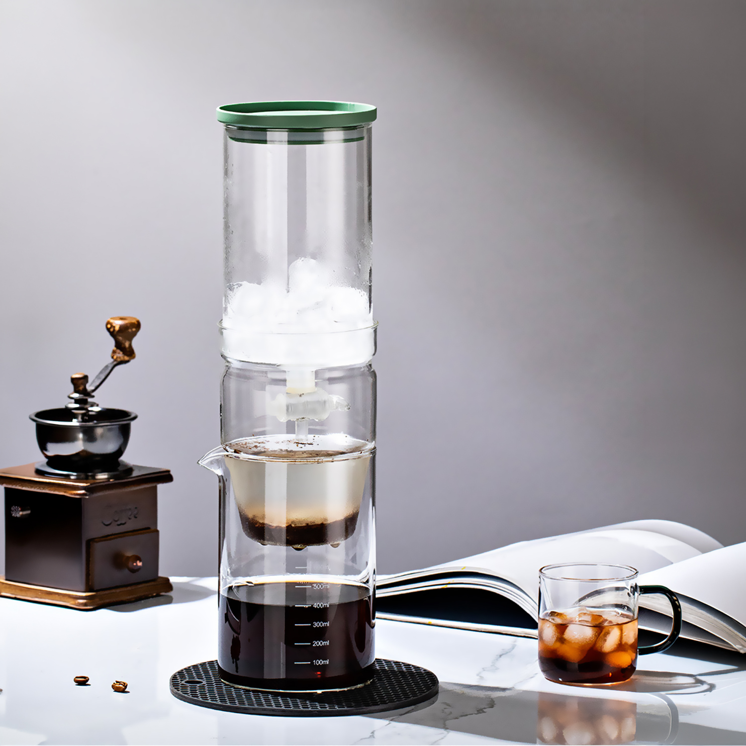 Una cafetera de infusión en frío con hielo, posos de café y un vaso de café helado.