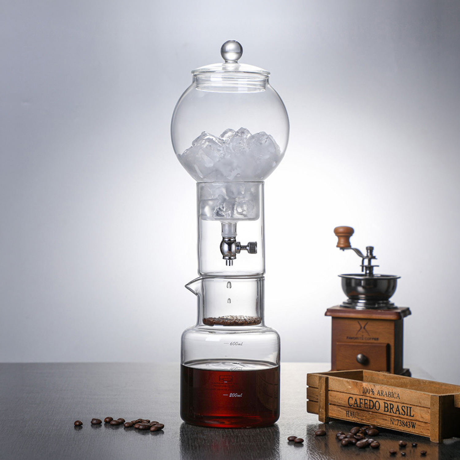 Cafetera de vidrio para café frío con hielo, granos de café y molinillo de madera.