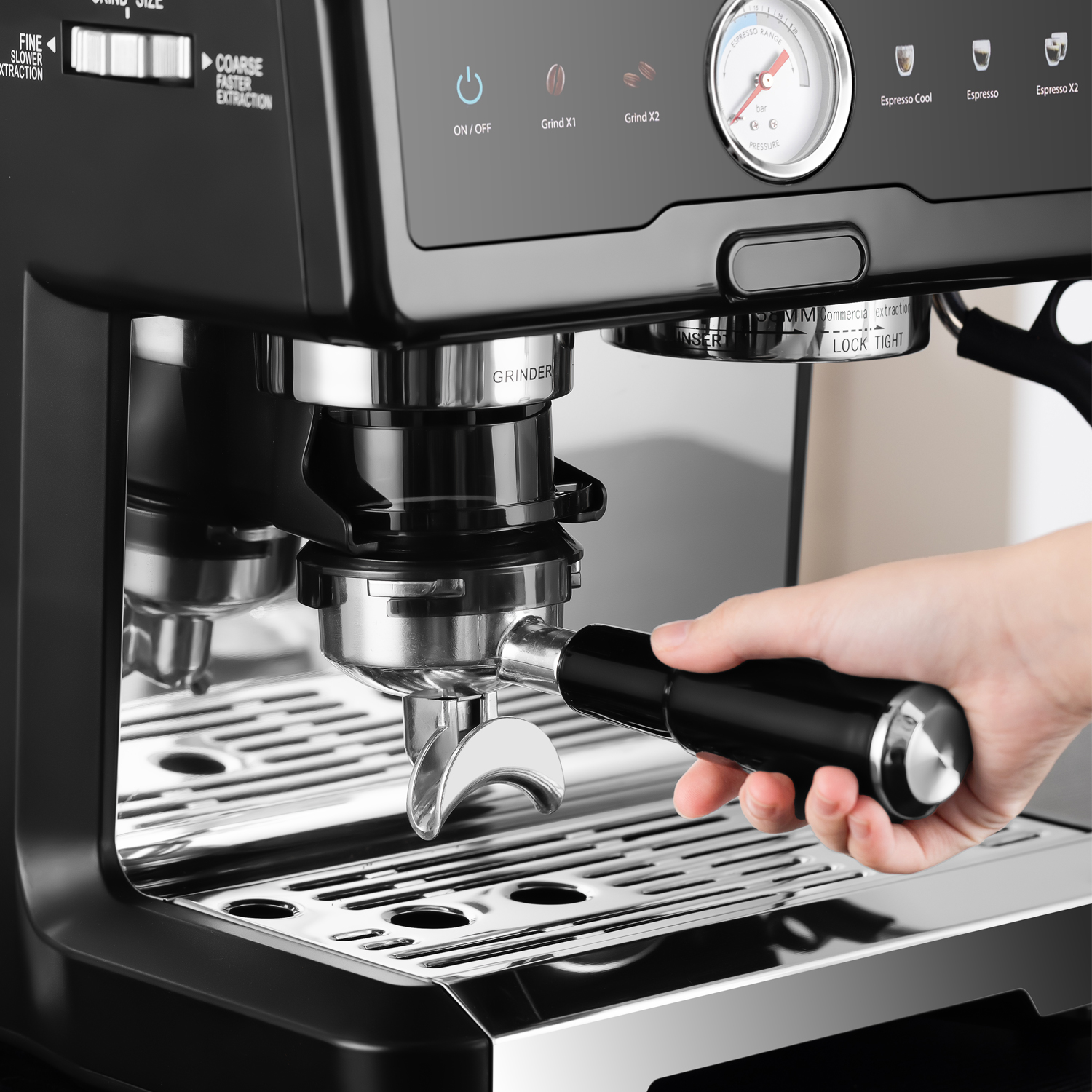 Hand hält schwarzen Siebträger einer Espressomaschine, schiebt ihn ein. Bedienelemente sichtbar.