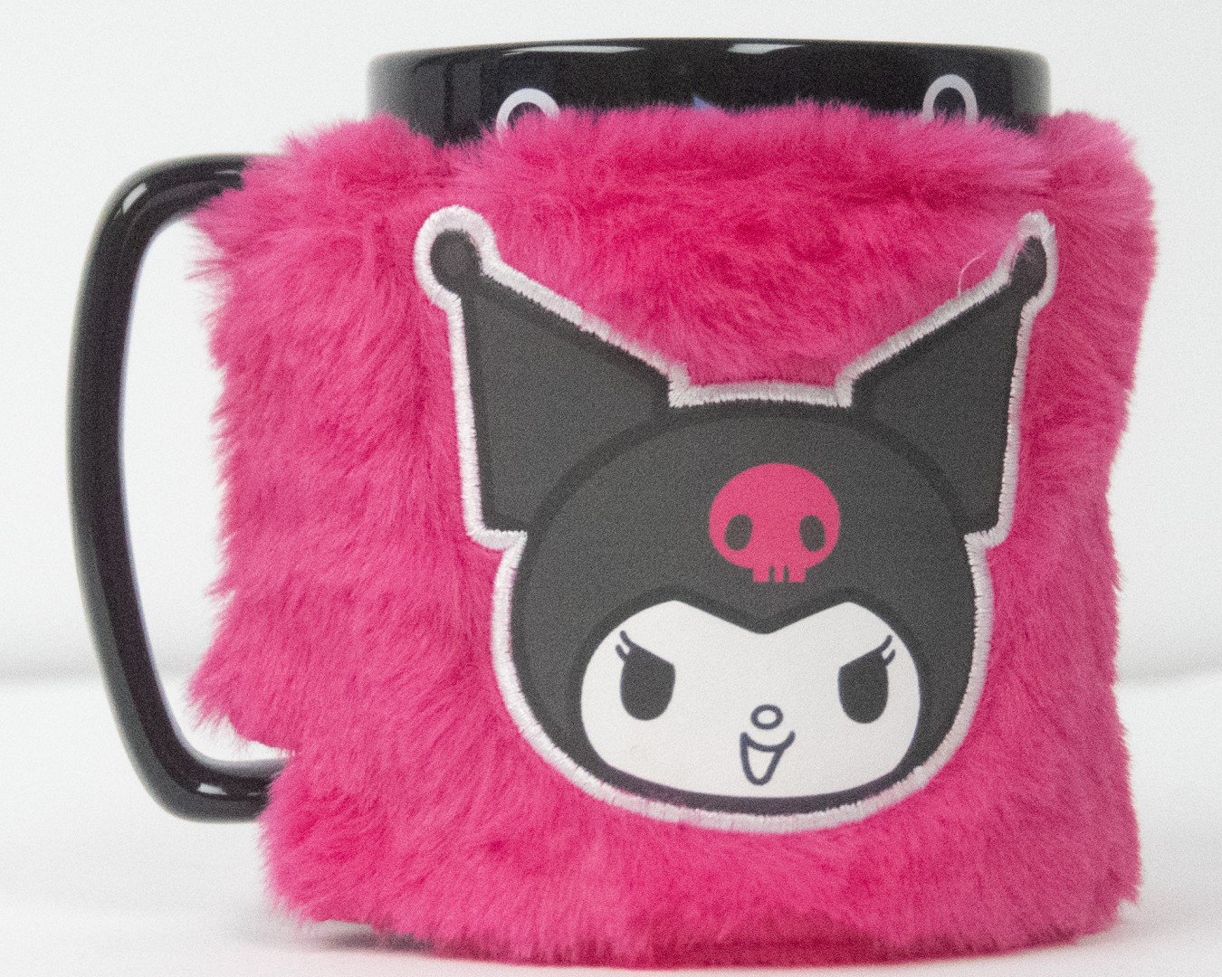 Una taza negra con una funda rosa peluda con la cara de Kuromi.