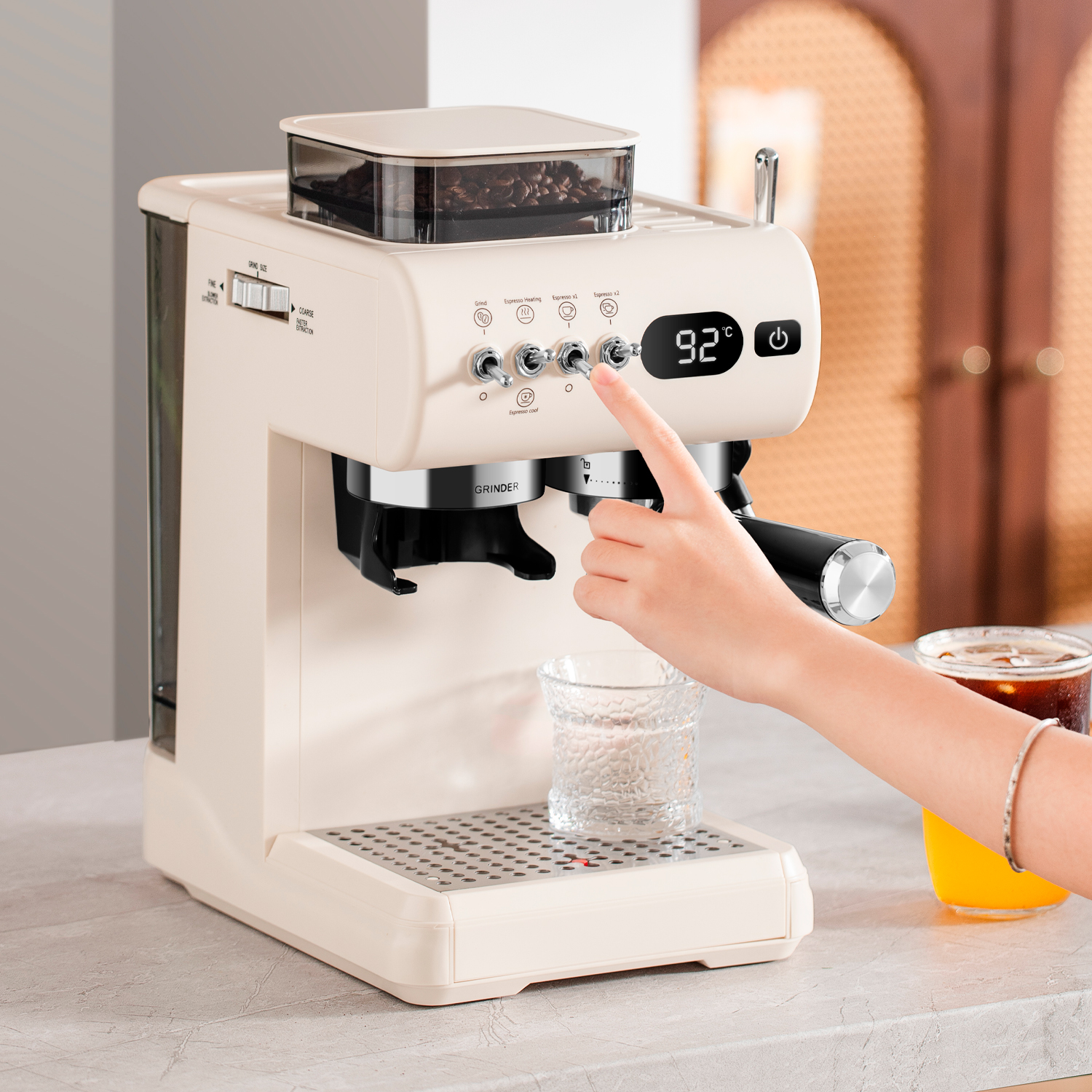 Eine Person bedient eine cremefarbene Espressomaschine mit Kaffeebohnen und einem Display.
