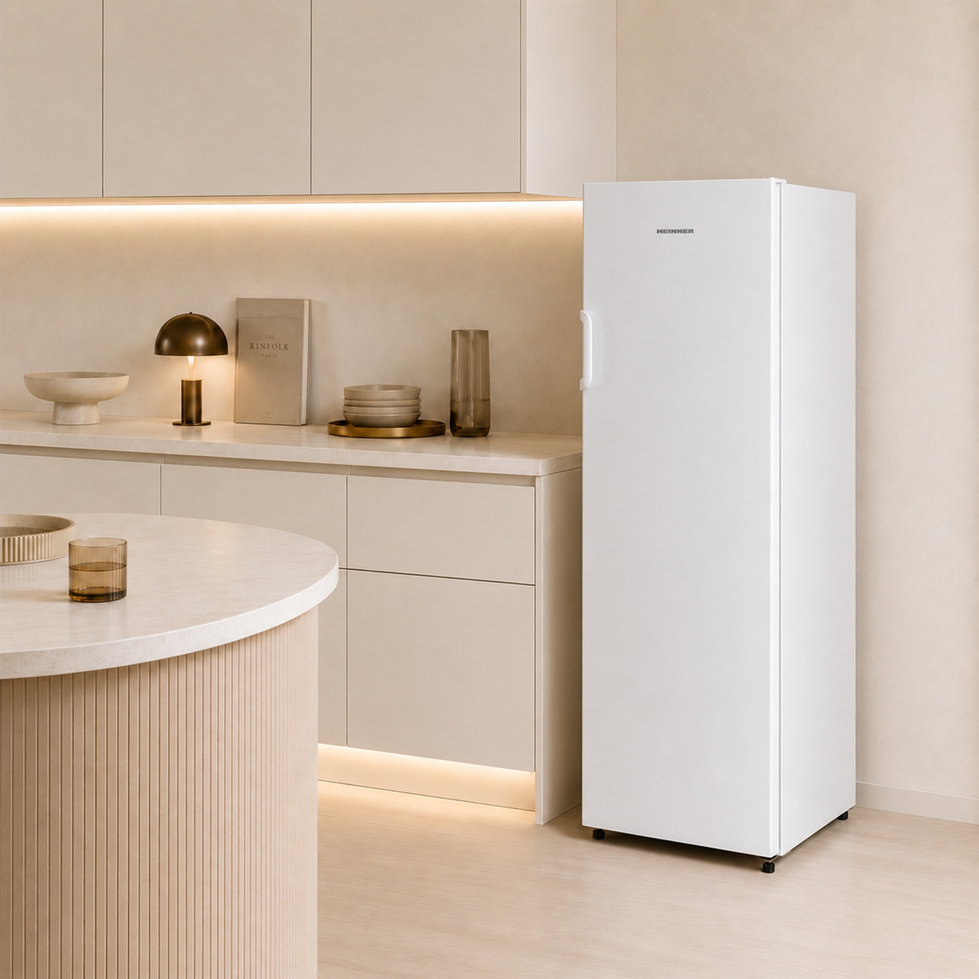 Ein weißer Heinner-Kühlschrank steht in einer modernen Küche mit hellbeigen Schränken.