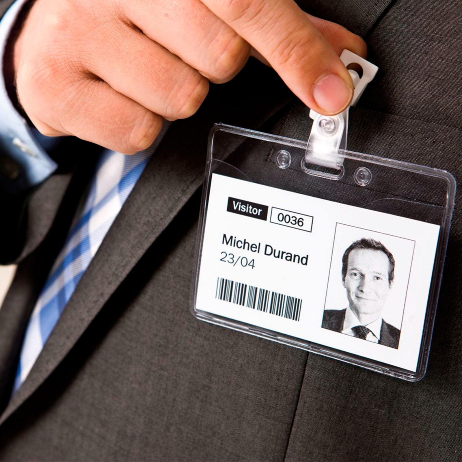 Un uomo in giacca e cravatta attacca un badge visitatore con foto, nome e codice.