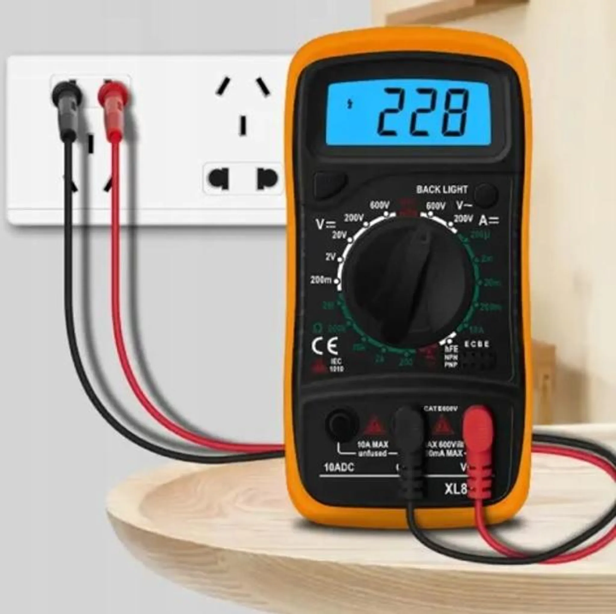 Ein oranges Multimeter mit blauer Anzeige (228) steckt in einer Steckdose.
