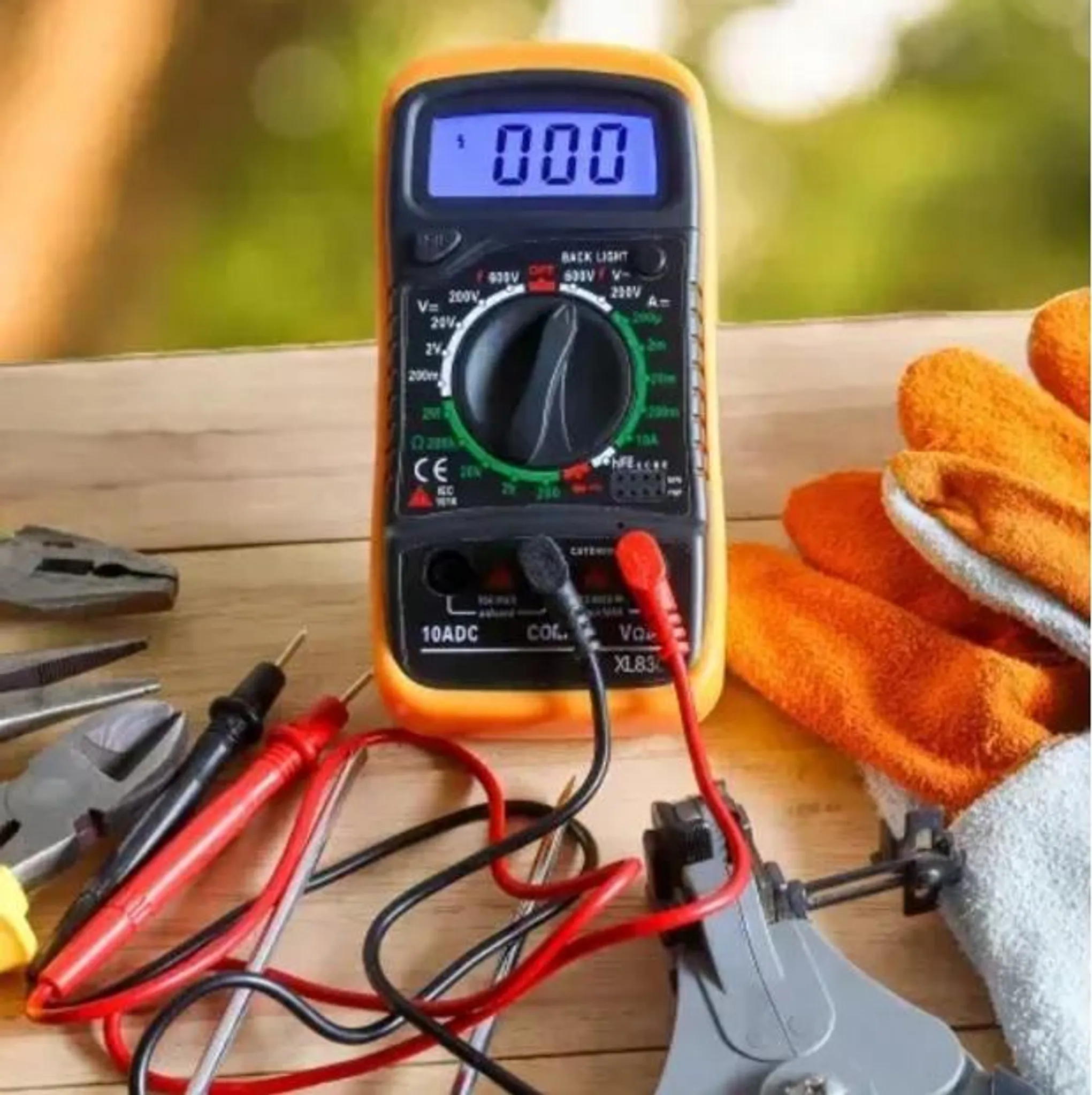 Ein Digitalmultimeter mit Prüfspitzen, Zange und Handschuhen auf einem Holztisch.