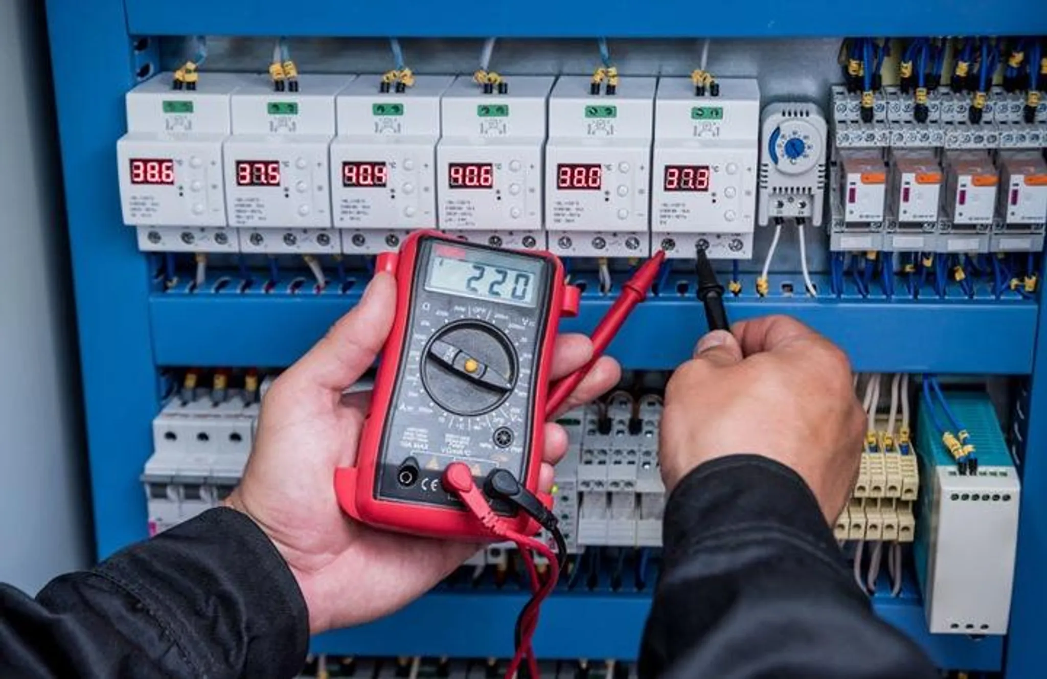 Ein Techniker misst Spannung an einem elektrischen Bedienfeld mit einem Multimeter.
