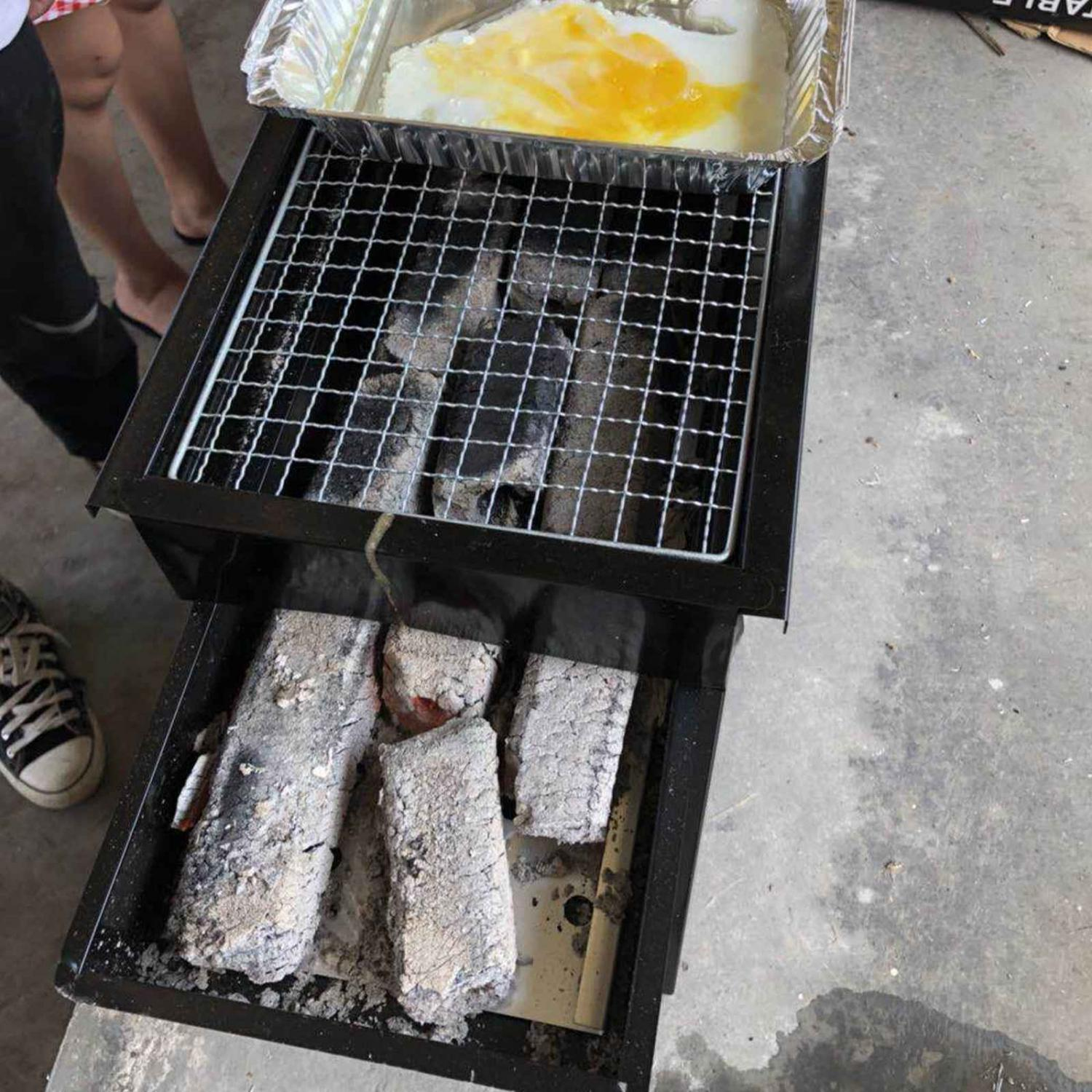 Ein Holzkohlegrill mit einer Alufolie für Rührei und einem Rost. Unten sind Kohlen sichtbar.