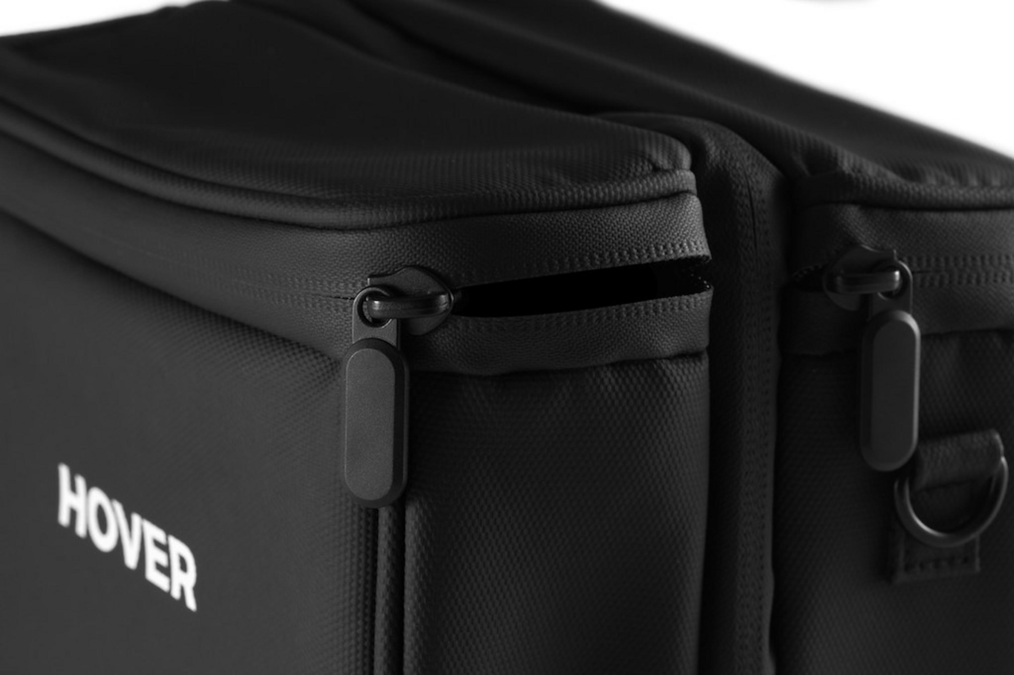 Bolso negro con cremalleras y el texto blanco HOVER. Vista cercana.