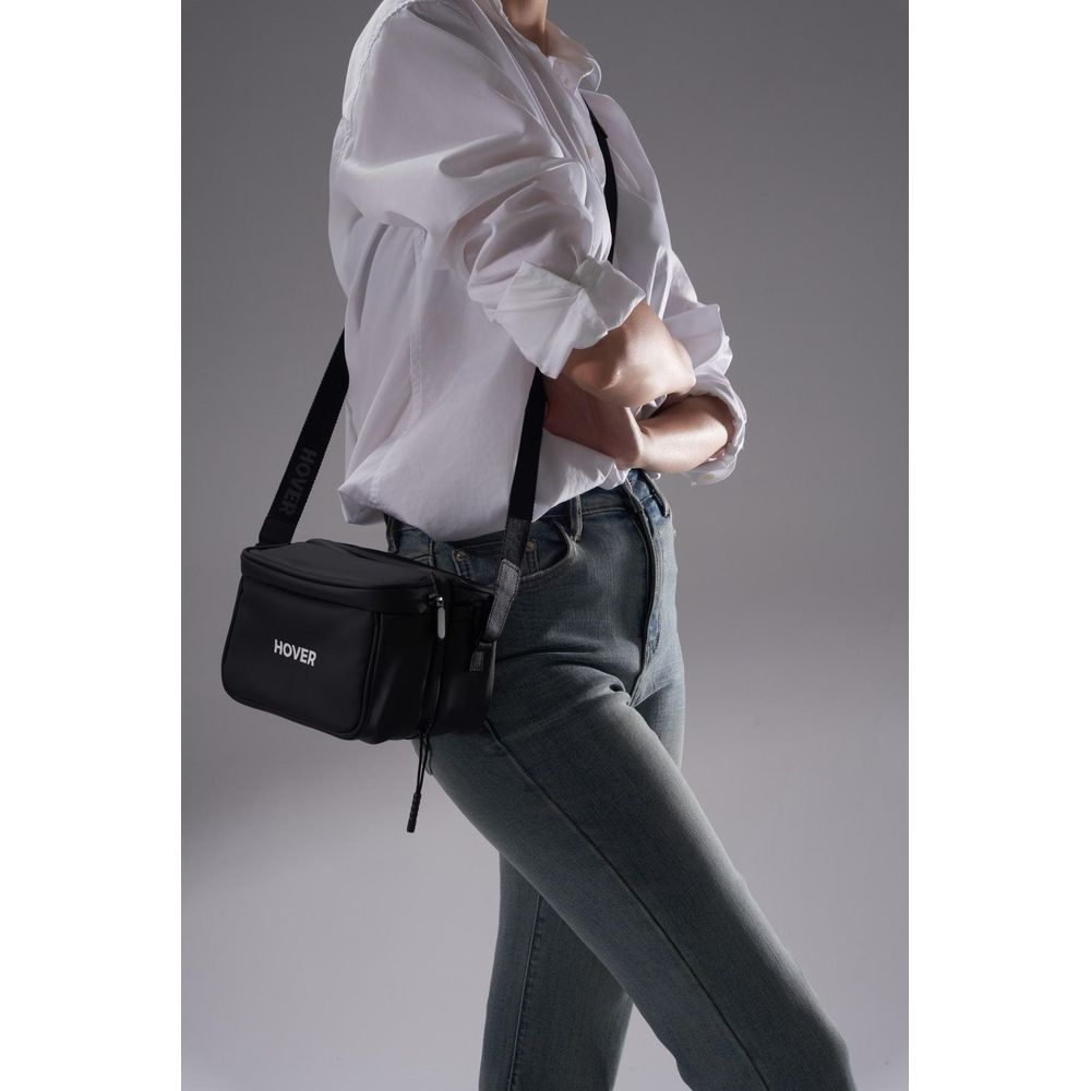Persona con camisa blanca y jeans lleva bolso cruzado negro con logo 'HOVER'.