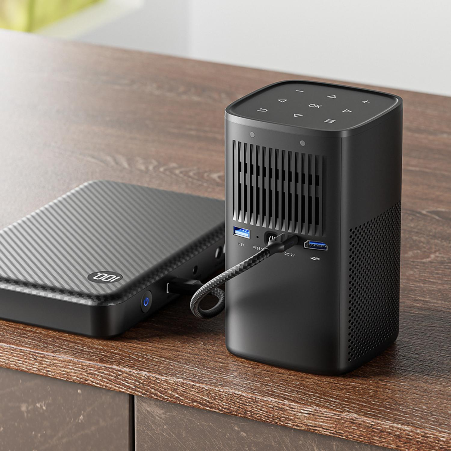 Schwarzer Projektor und Powerbank mit Karbonfasertextur auf Holztisch.