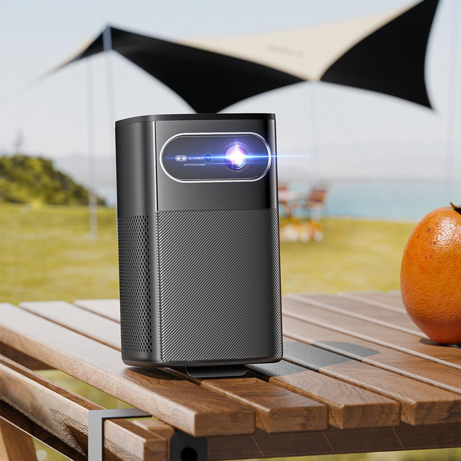 Schwarzer Projektor auf Holztisch mit Orange und Campingzelt im Hintergrund.