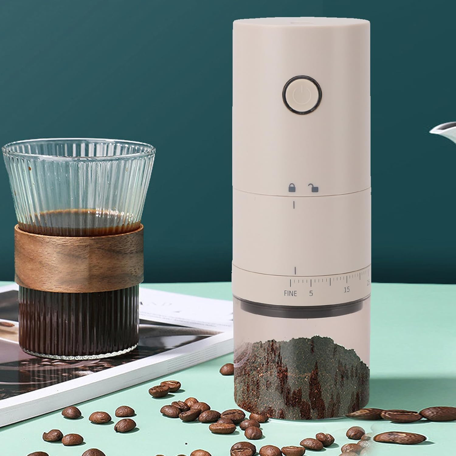 Un molinillo de café eléctrico beige junto a un vaso de café, con granos esparcidos.