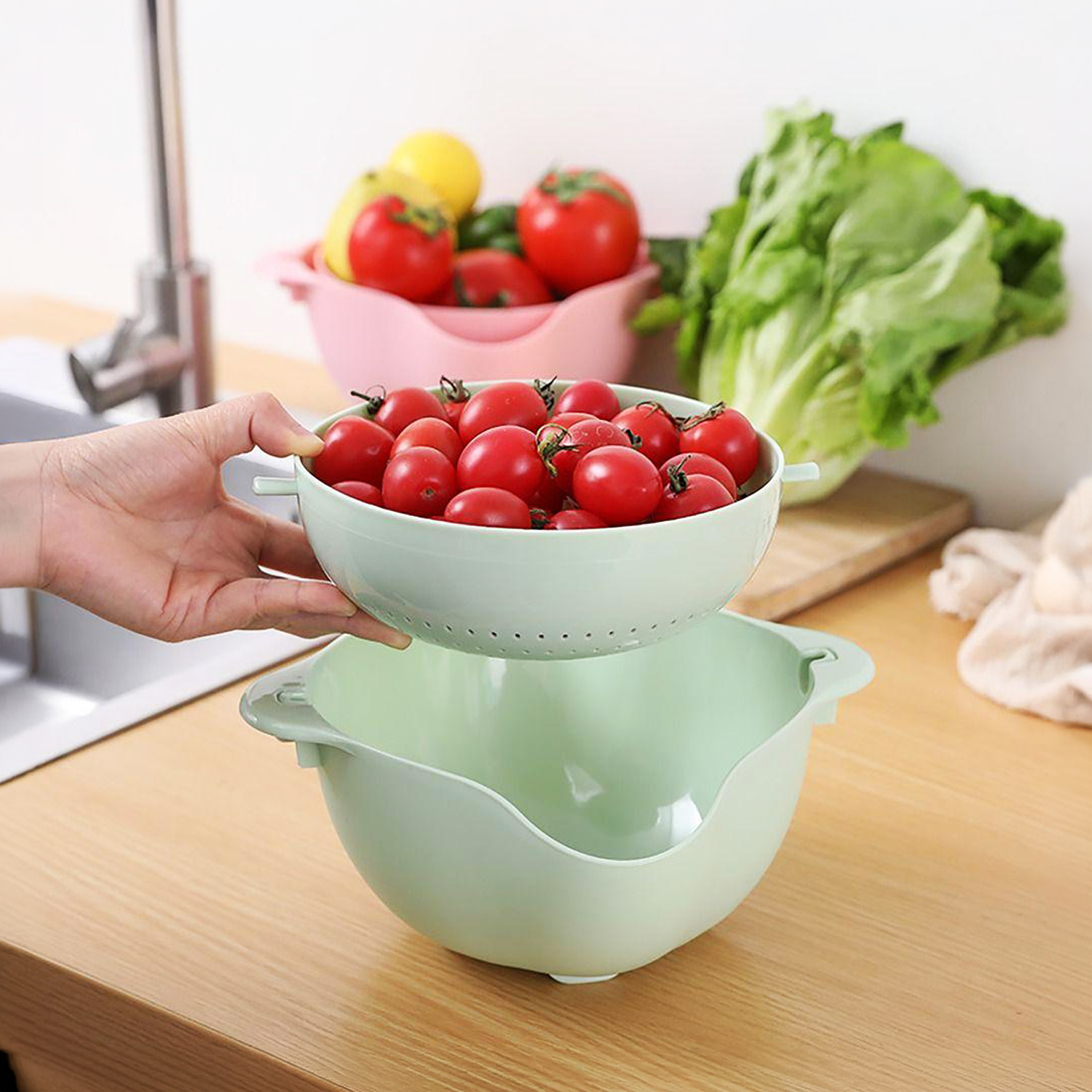 Eine Hand hält ein hellgrünes Sieb mit roten Kirschtomaten über einer passenden Schüssel.