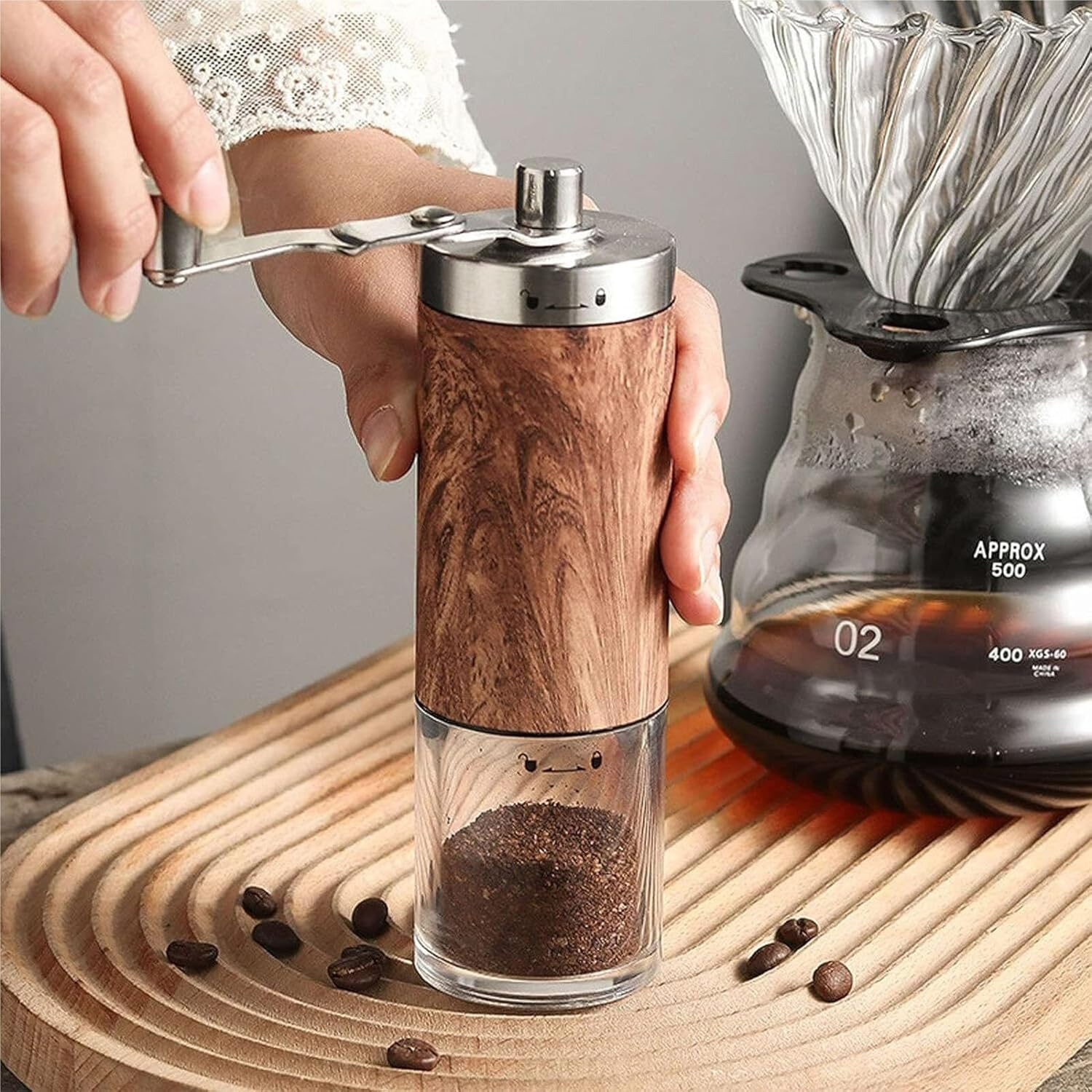 Una mano muele café en un molinillo de madera junto a una cafetera.