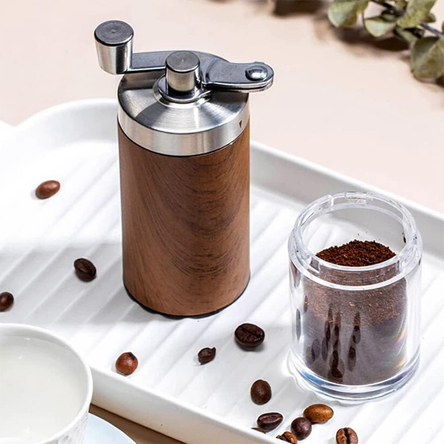Molinillo de café de madera y metal junto a una taza de café molido y granos.