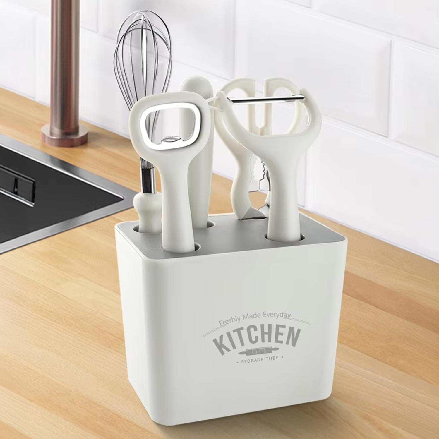 Küchenutensilienhalter mit weißem Gehäuse und Edelstahlwerkzeugen wie Schneebesen und Sparschäler.