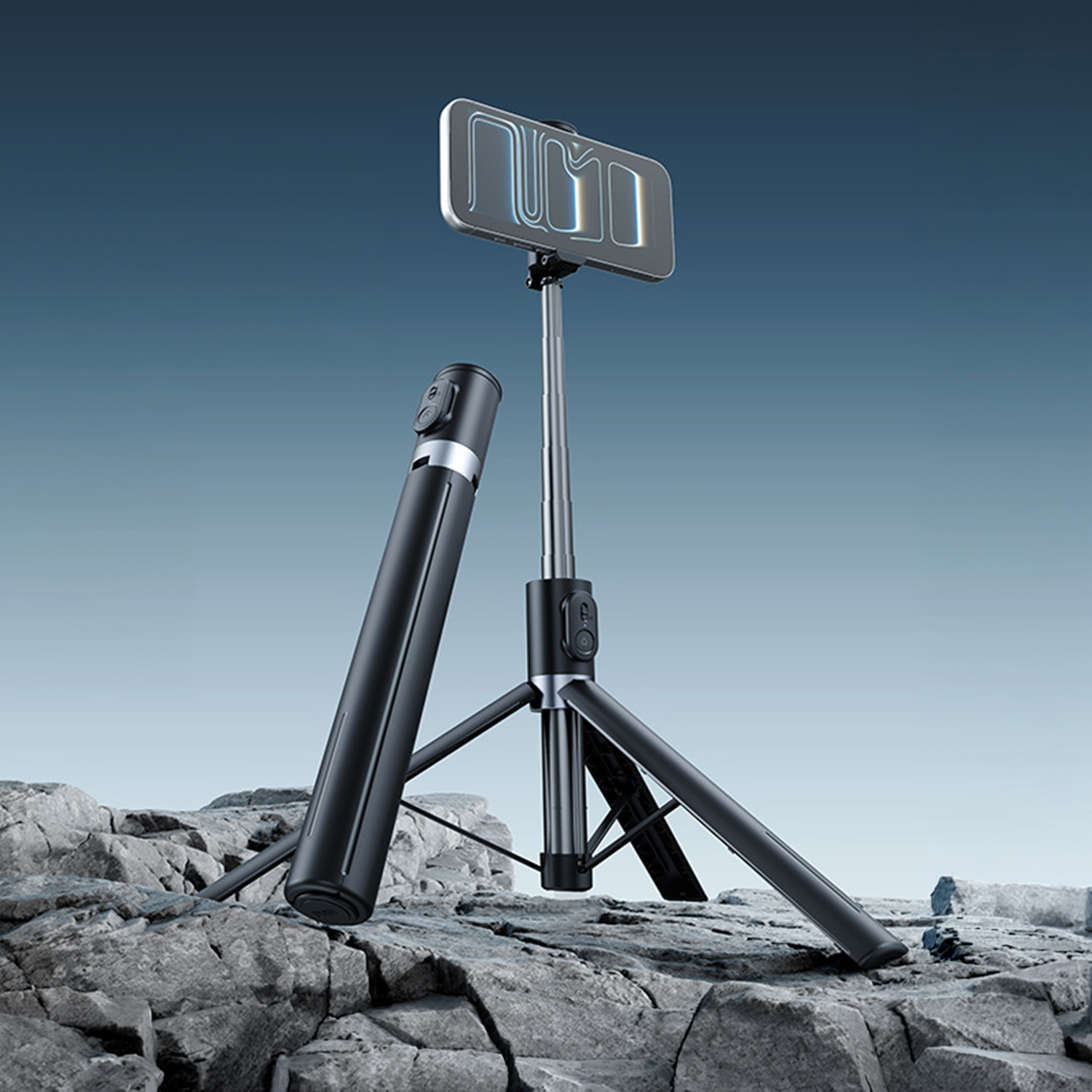 Ein schwarzer Selfie-Stick mit ausklappbarem Stativ und Handyhalterung steht auf Felsen.