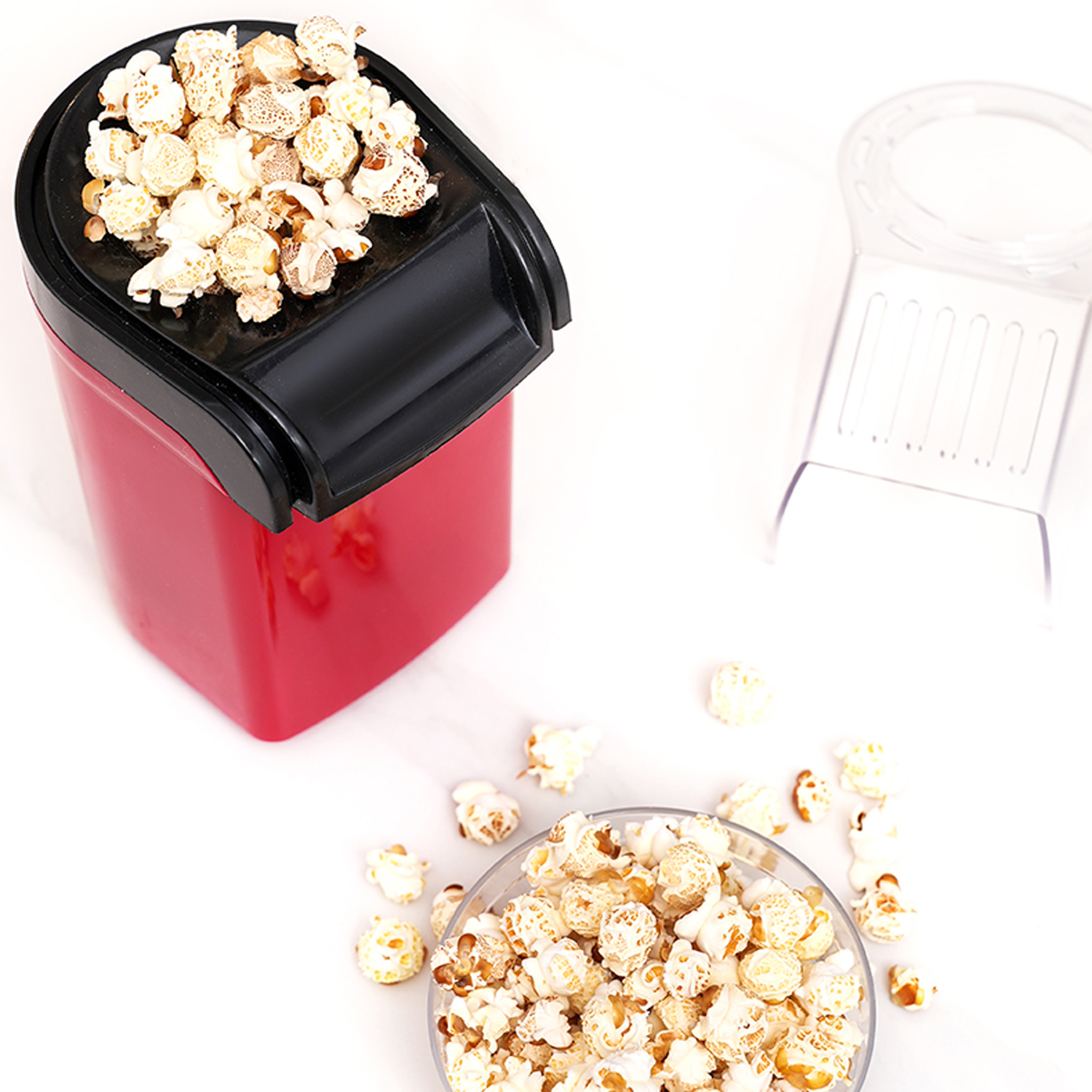 Máquina de palomitas roja con tapa negra, cubierta de palomitas. Un cuenco de palomitas cerca.