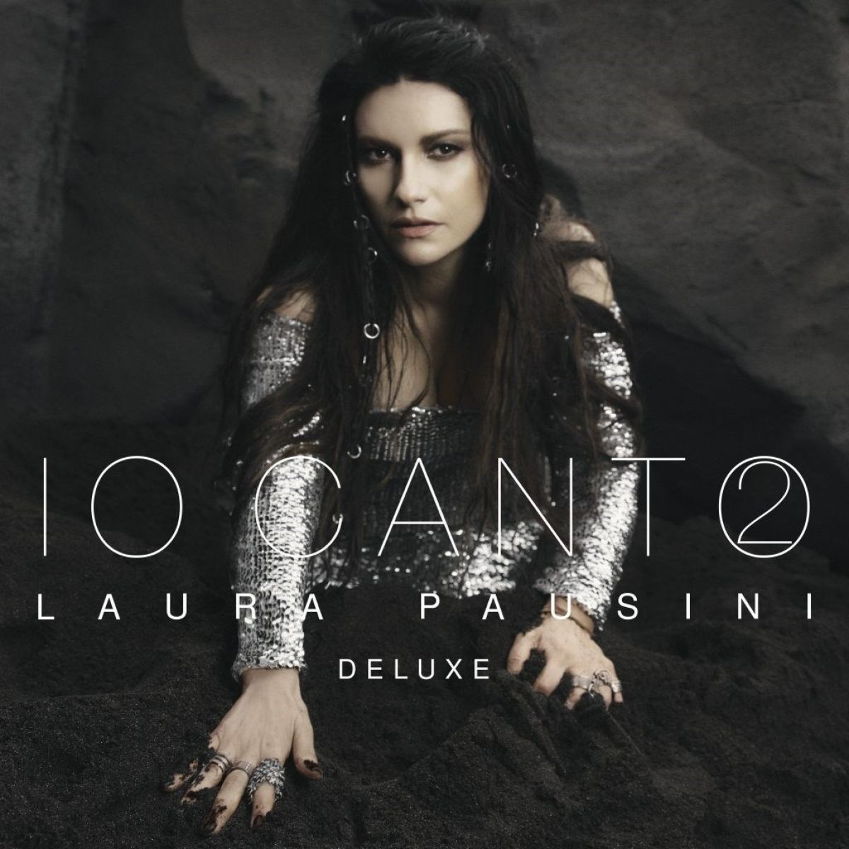 Laura Pausini su sfondo scuro e terroso, indossa un top scintillante.