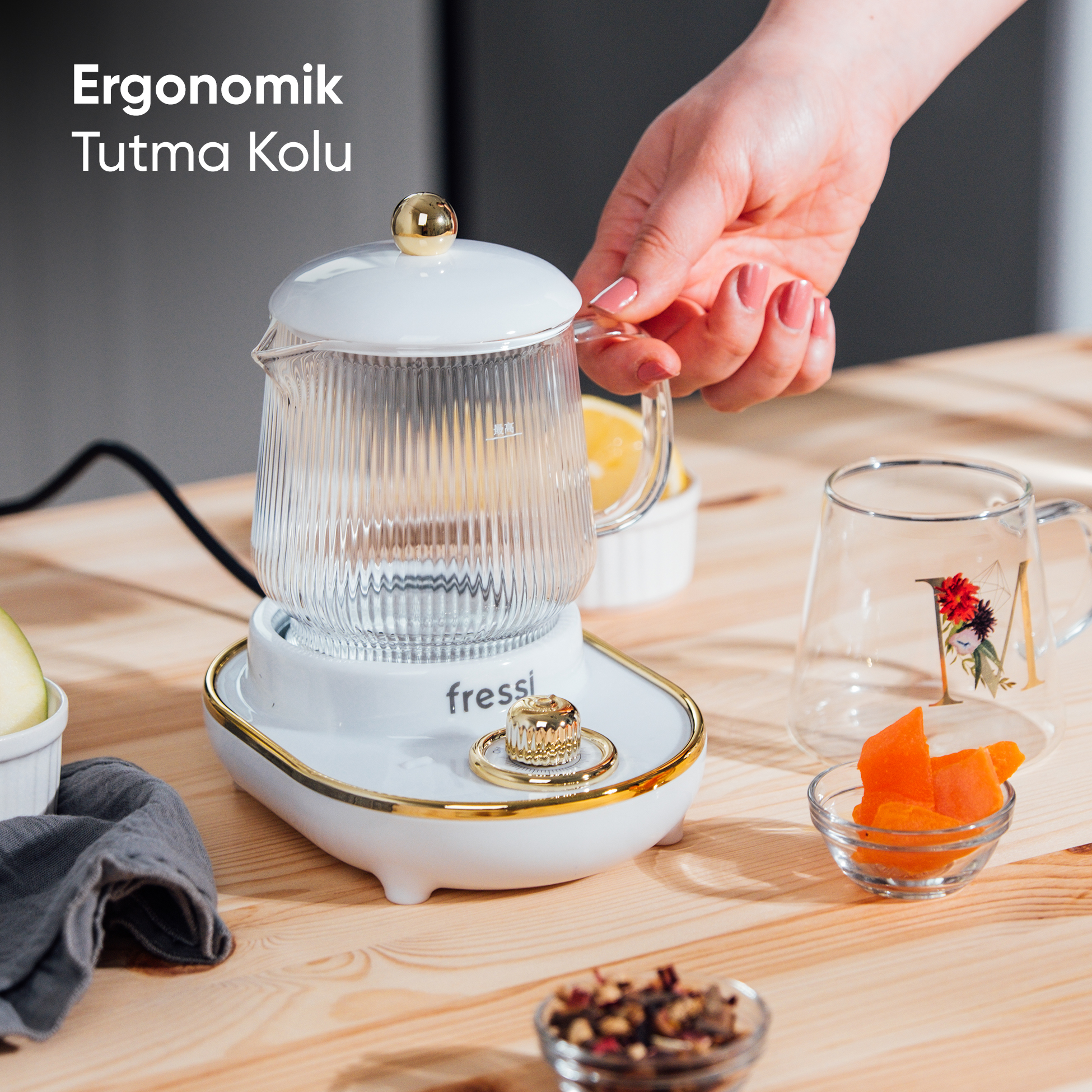 Altın aksesuarlı beyaz bir demliğin üzerinde bir el cam kapak tutuyor.