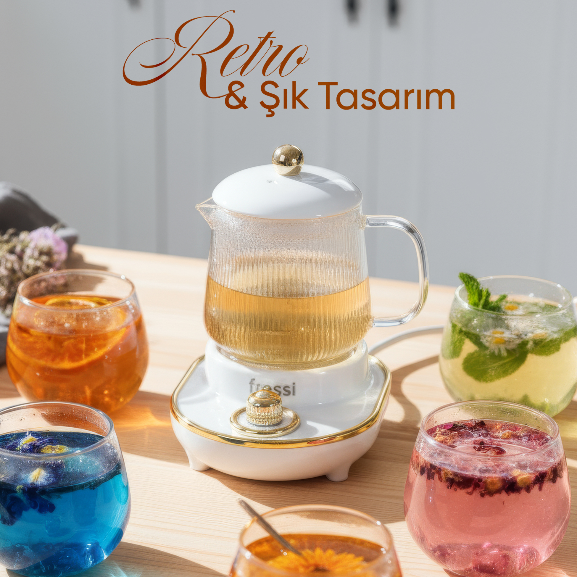 Altın topuzlu cam demlik, renkli içeceklerle çevrili beyaz bir tabanda duruyor.