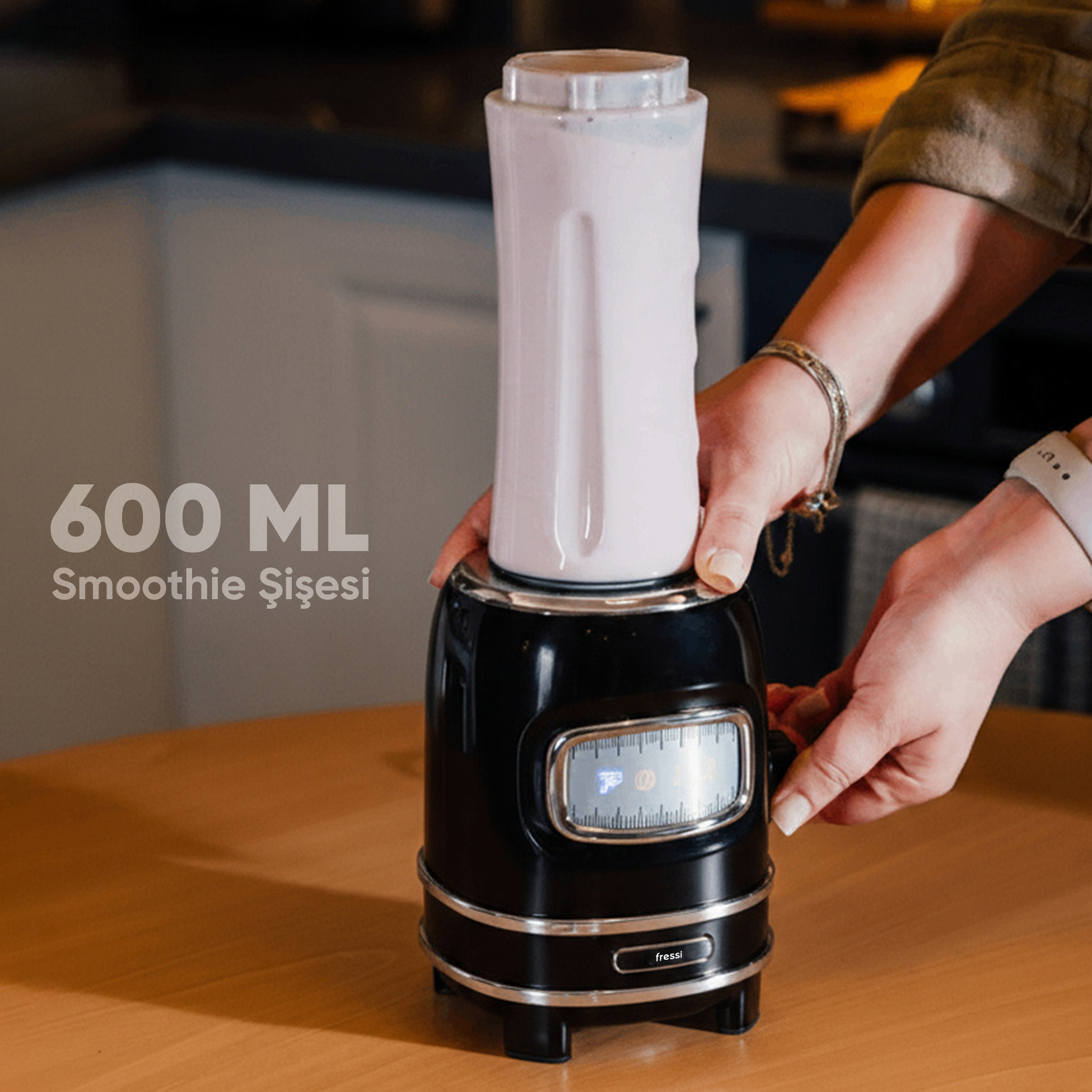 Kişi, 600 ml kapasiteli beyaz haznesi olan siyah blenderi kullanıyor.