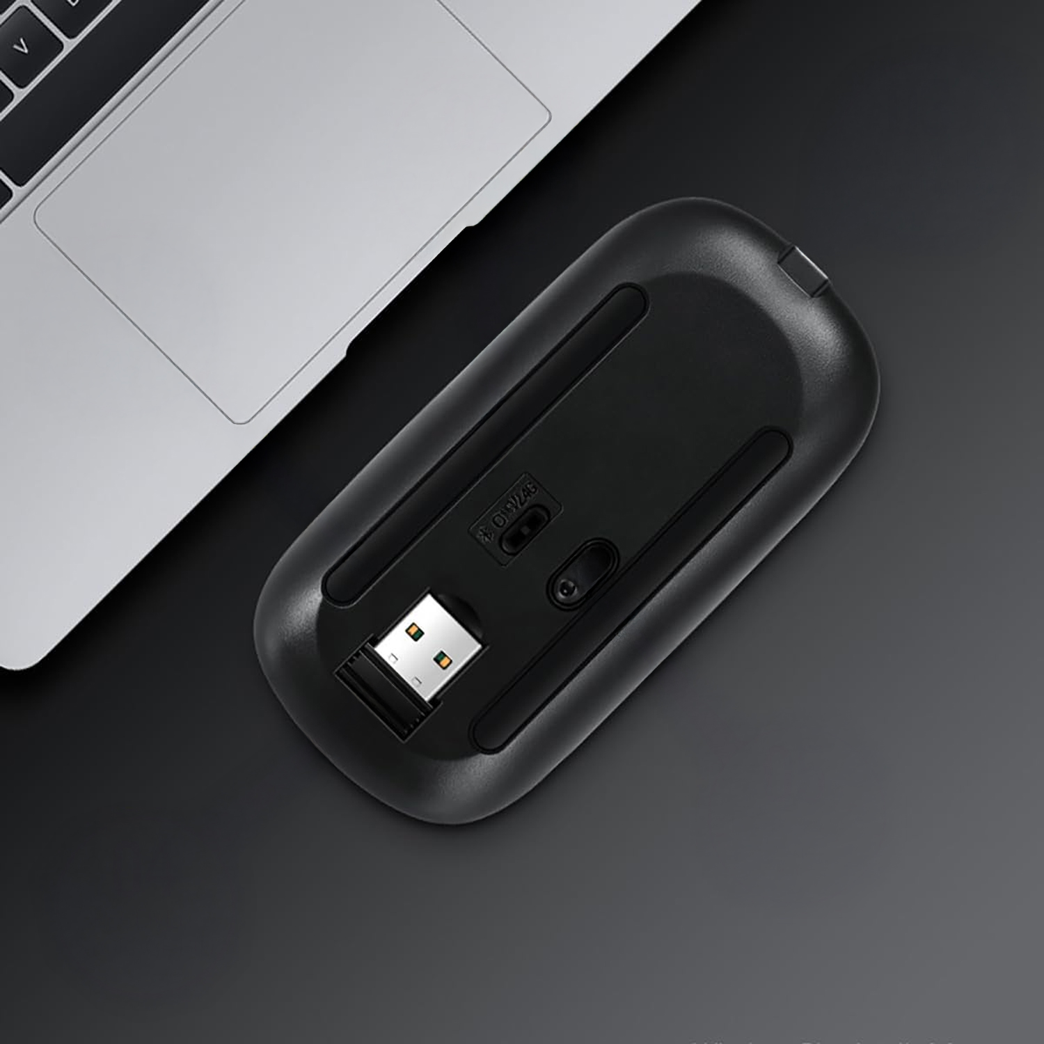 Un ratón negro con dongle USB descansa junto a un portátil.