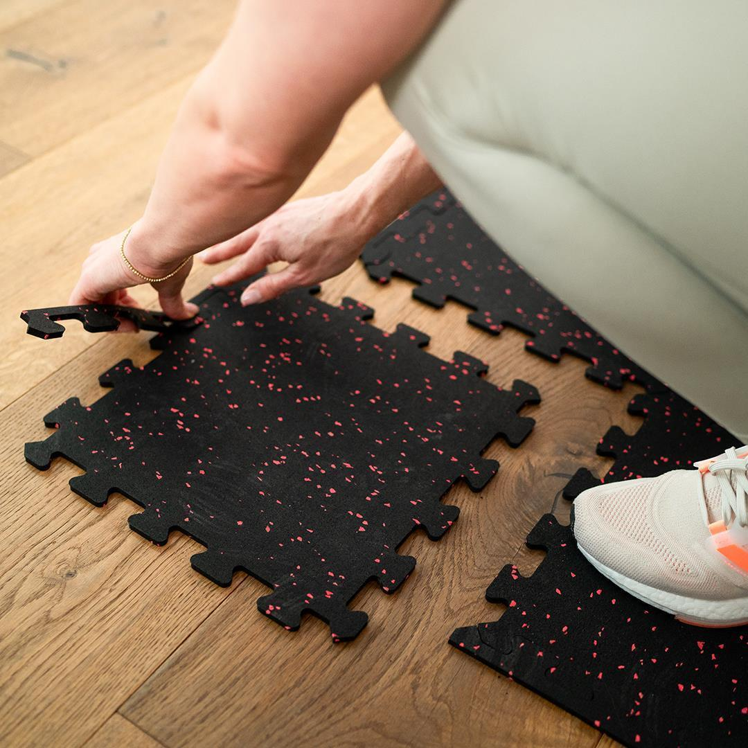 Schwarze Fitnessmatten mit roten Sprenkeln werden auf Holzboden verlegt.