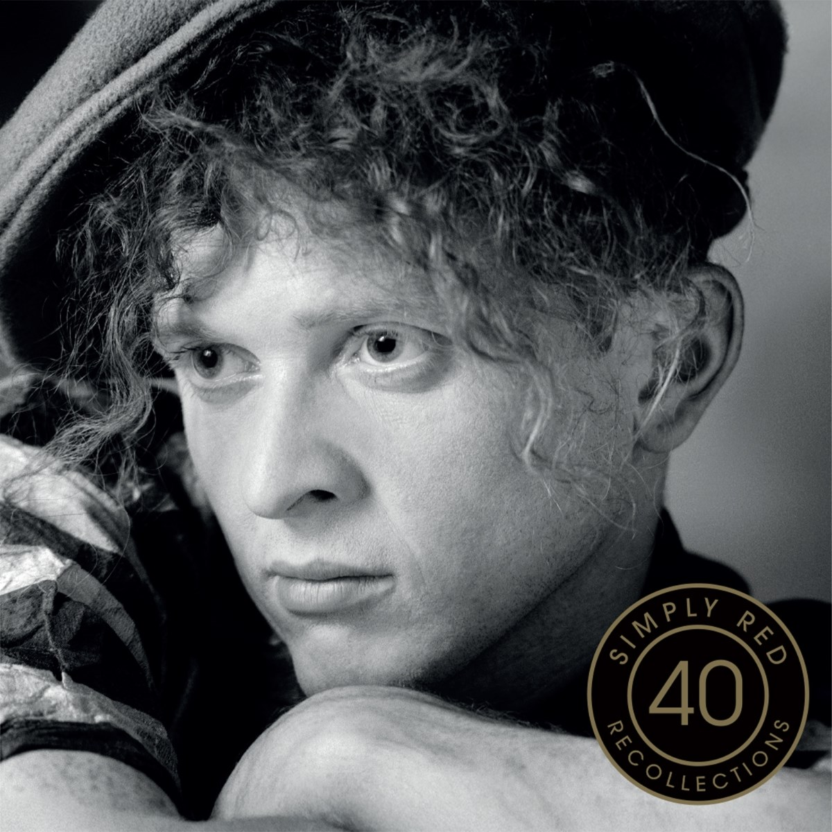 Primo piano in bianco e nero di un uomo con capelli ricci e cappellino. Logo Simply Red.