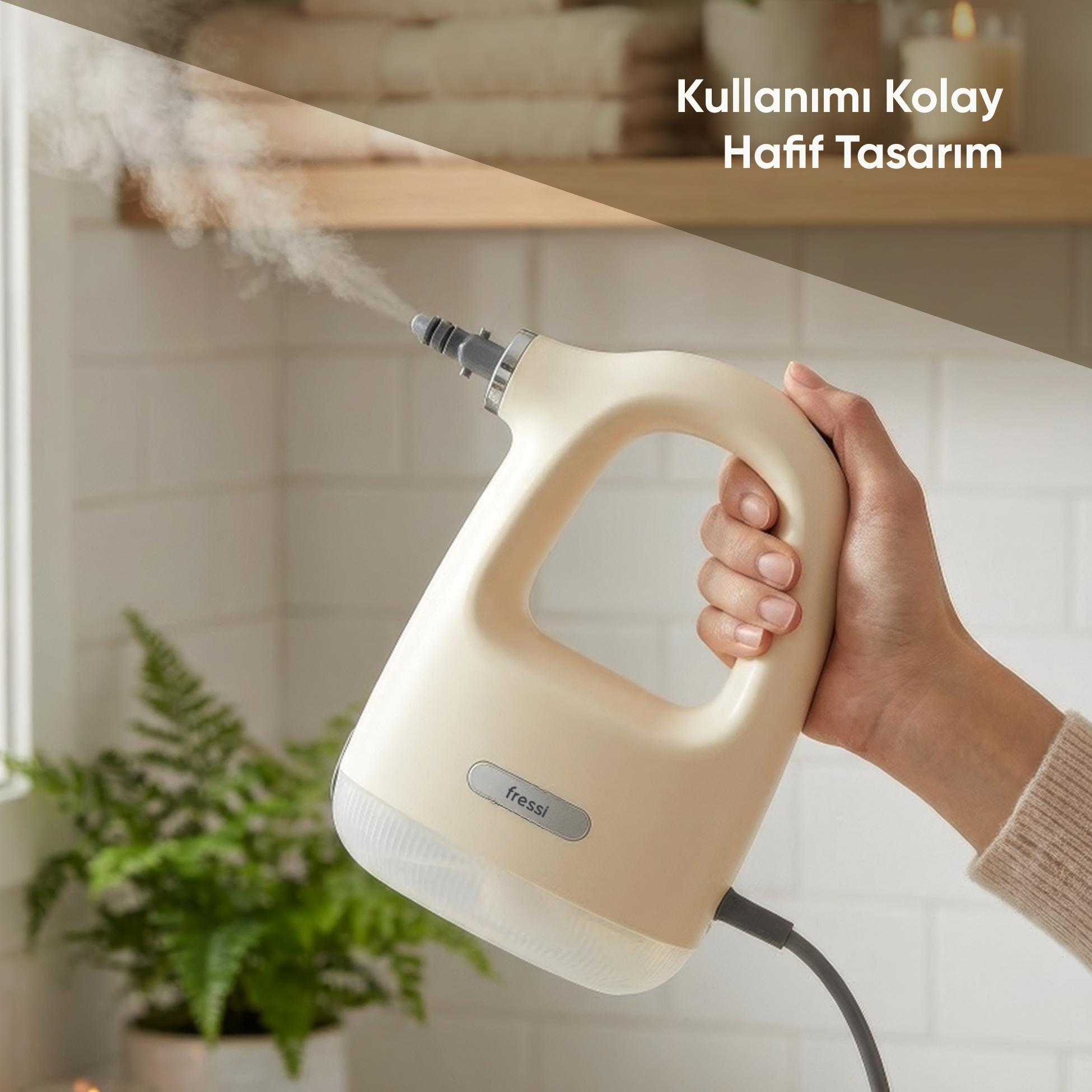 Bir el, buhar yayan krem rengi el tipi buharlı temizleyici tutuyor. Arkada eğrelti otu var.