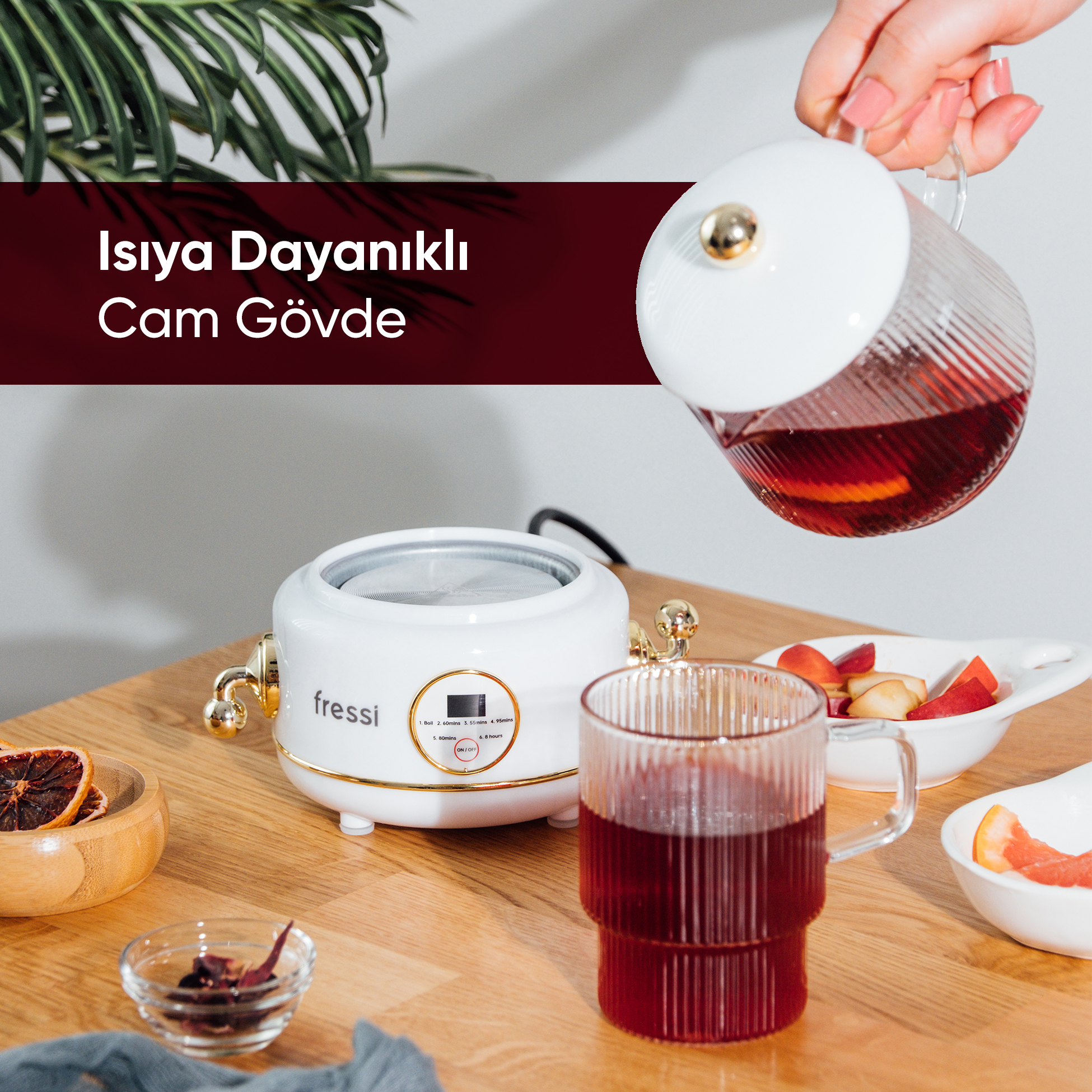 Bir el, cam demlikten kırmızı çayı, beyaz bir cihazın yanındaki yivli bardağa döküyor.