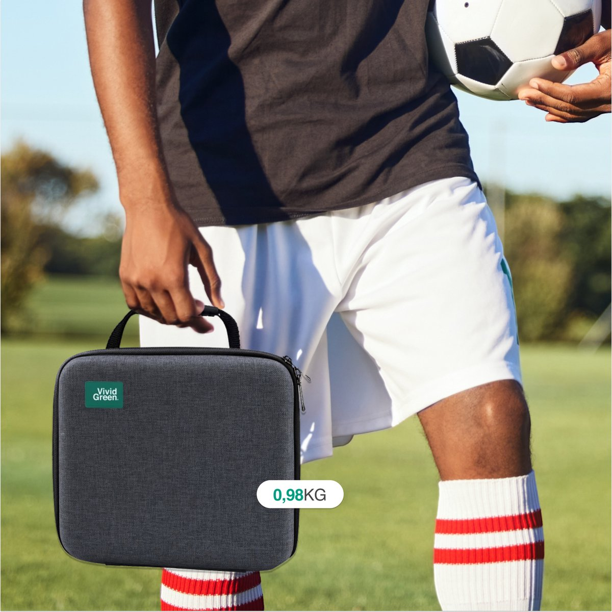 Man in soccer uniform holds a black case and a soccer ball on a field.
