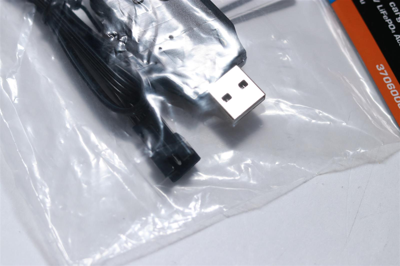 Ein USB-Kabel mit silbernem Stecker und schwarzen Kabeln in Plastikverpackung.